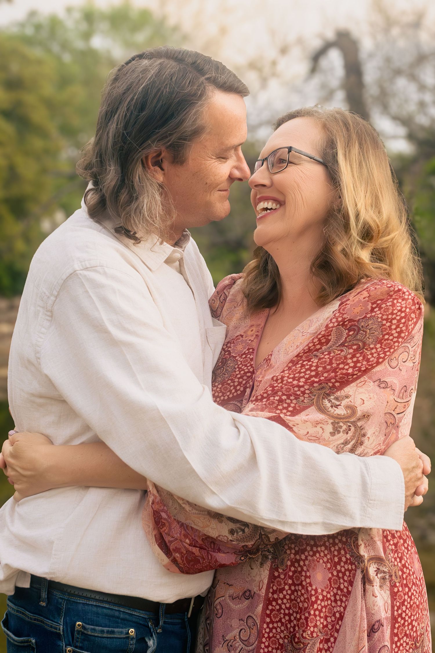 A romantic outdoor portrait of a couple embracing and laughing together, with soft lighting and natural scenery in Fort Worth, Texas.