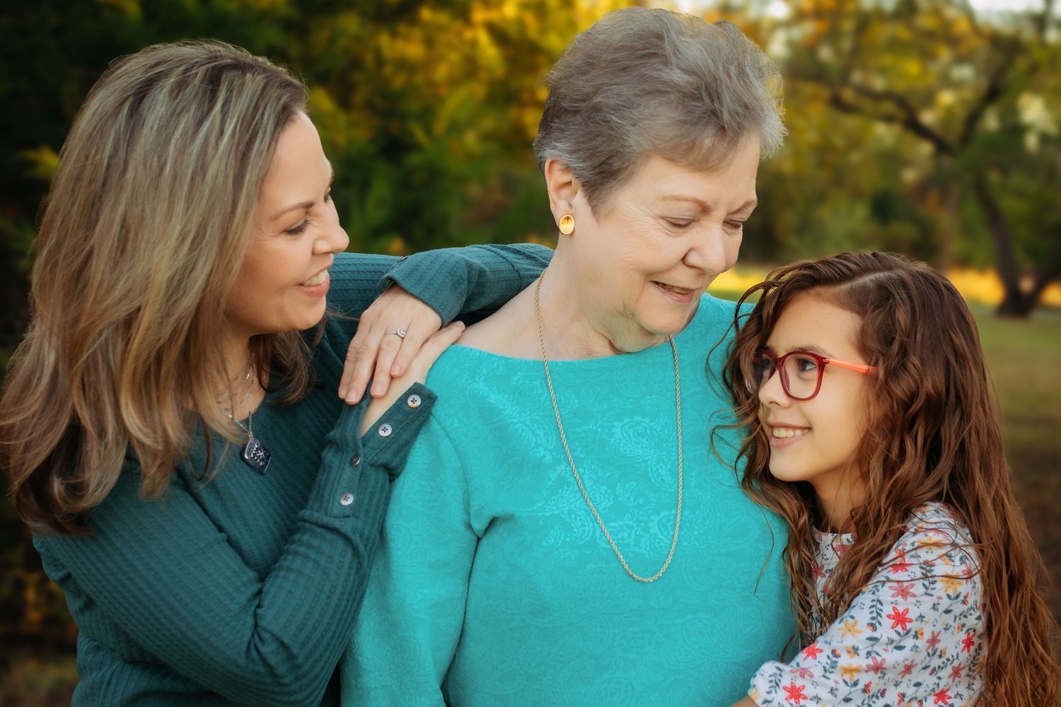 Three generations share loving embraces and laughter in an outdoor fall setting.