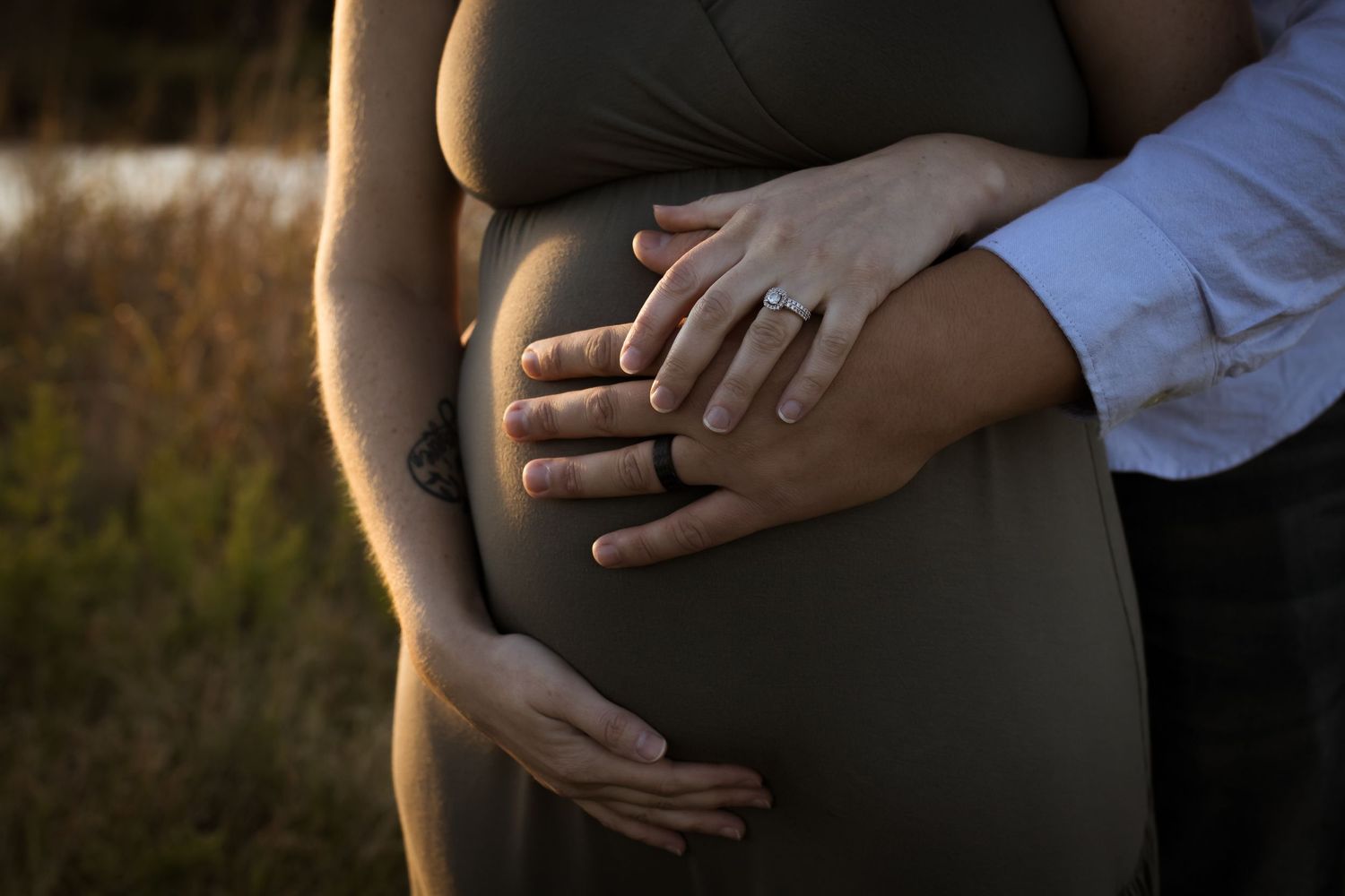 Close-up of hands cradling pregnant belly during sunset maternity session.