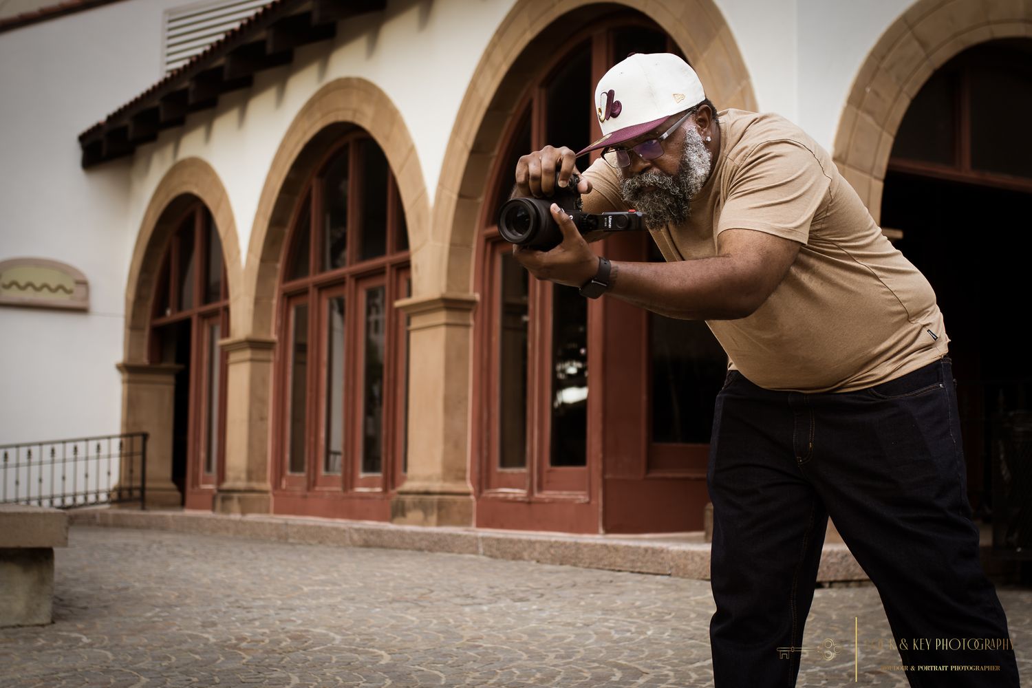 Photographer in khaki shirt and hat taking photos in front of Spanish colonial architecture.