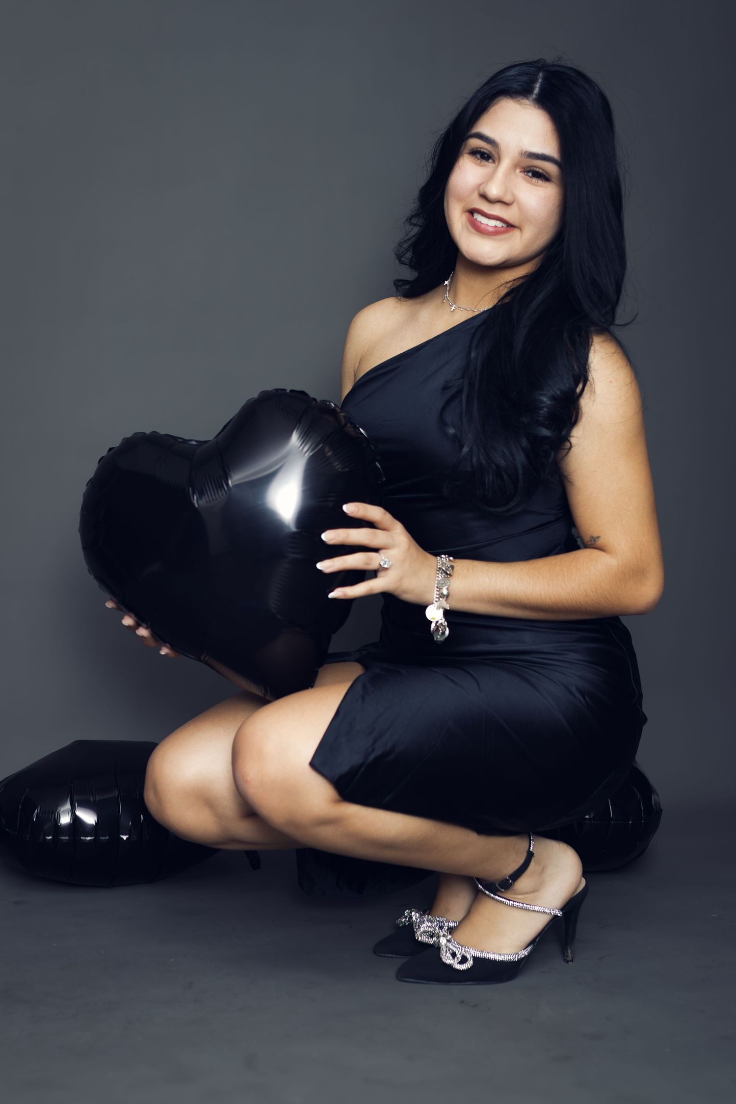A glamorous portrait of a woman in black holding a heart shaped balloon.