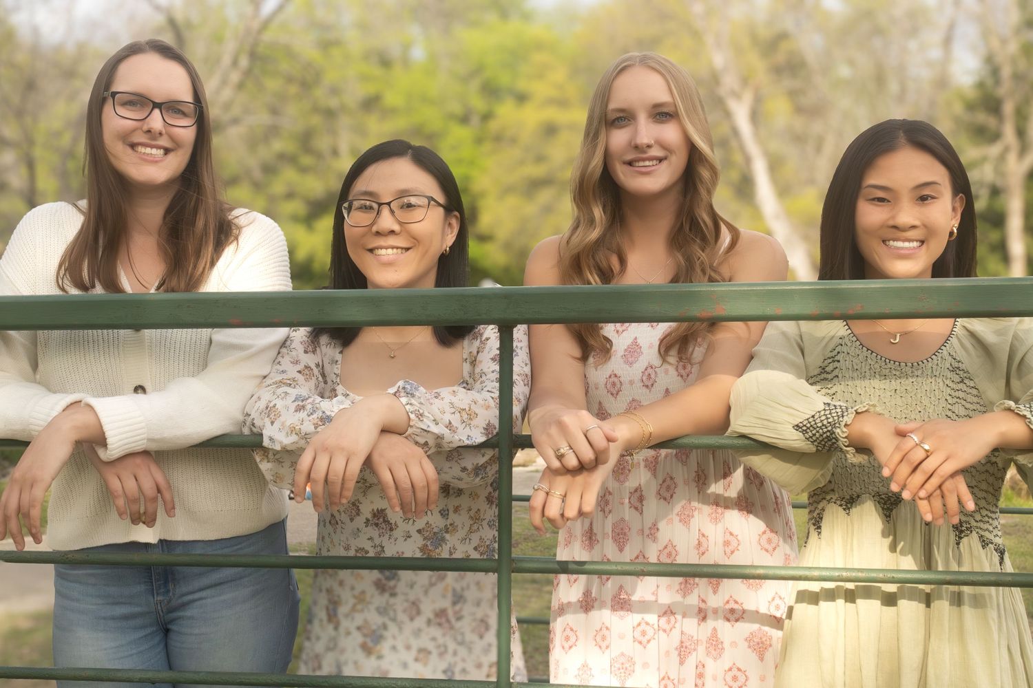 A group of four sisters smile while leaning on green railings outdoors during a family photography session in Fort Worth, Texas.