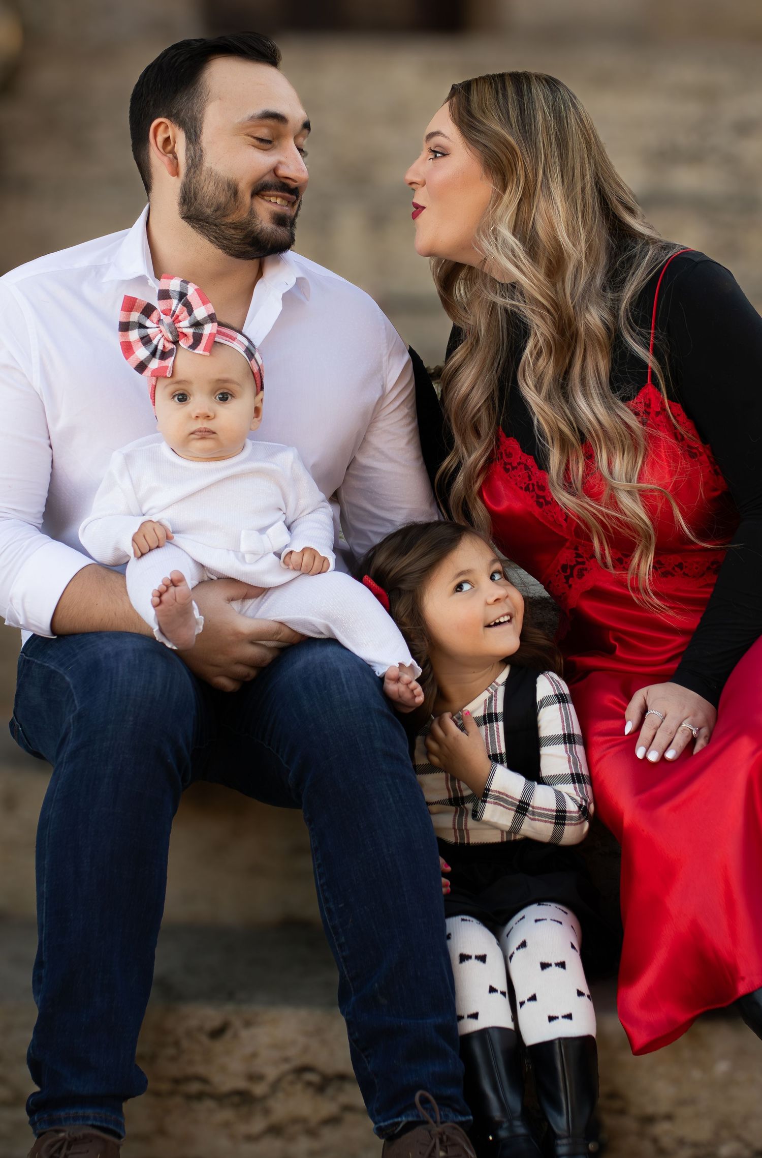 Happy family portrait with parents in casual attire and children sitting on stone steps.