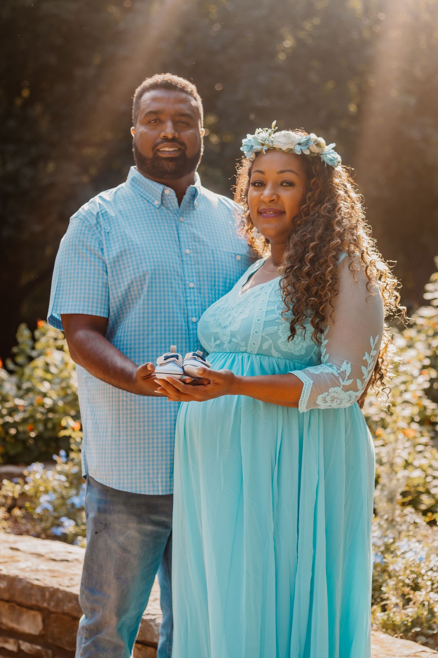Couple in coordinating blue outfits smiling in golden sunlight during outdoor maternity photo session.