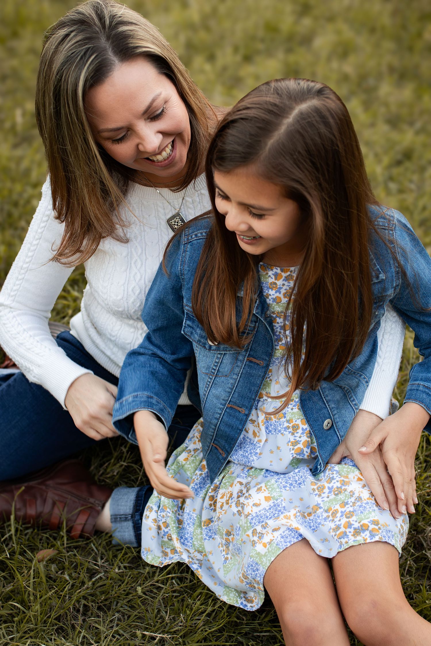 Two people share a genuine laugh while sitting together on grass outdoors.