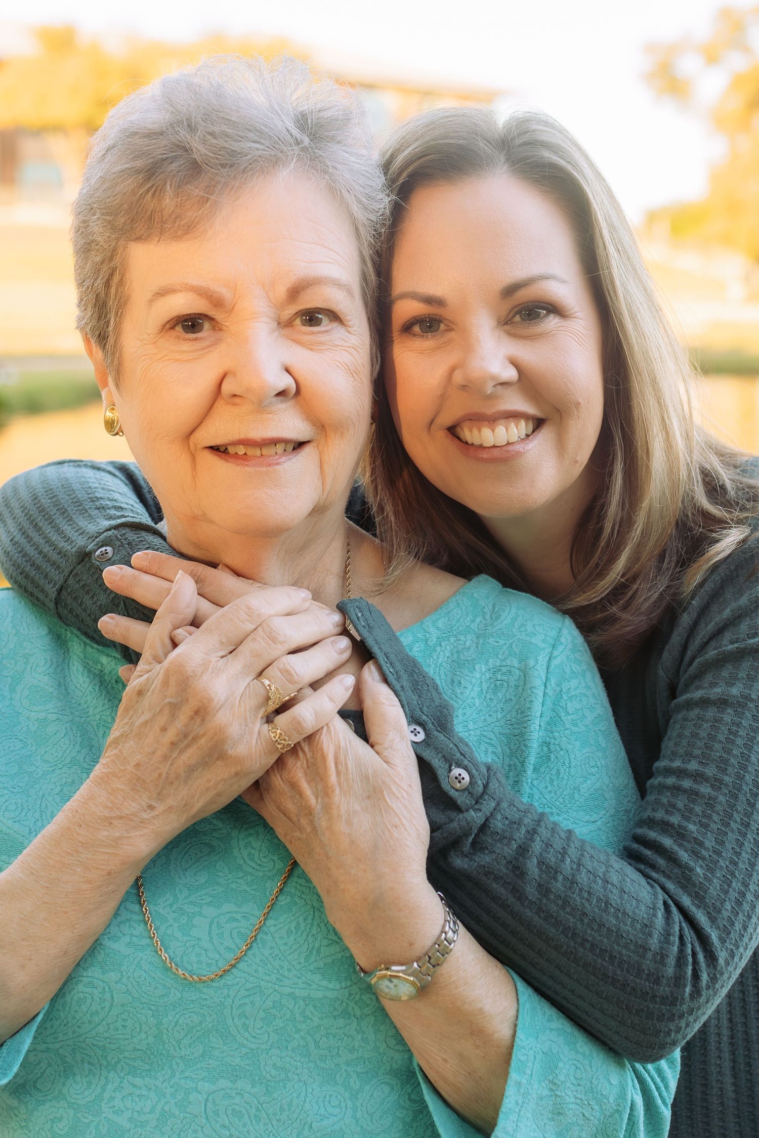 A tender moment captured between two women in turquoise and dark sweaters against autumn foliage.