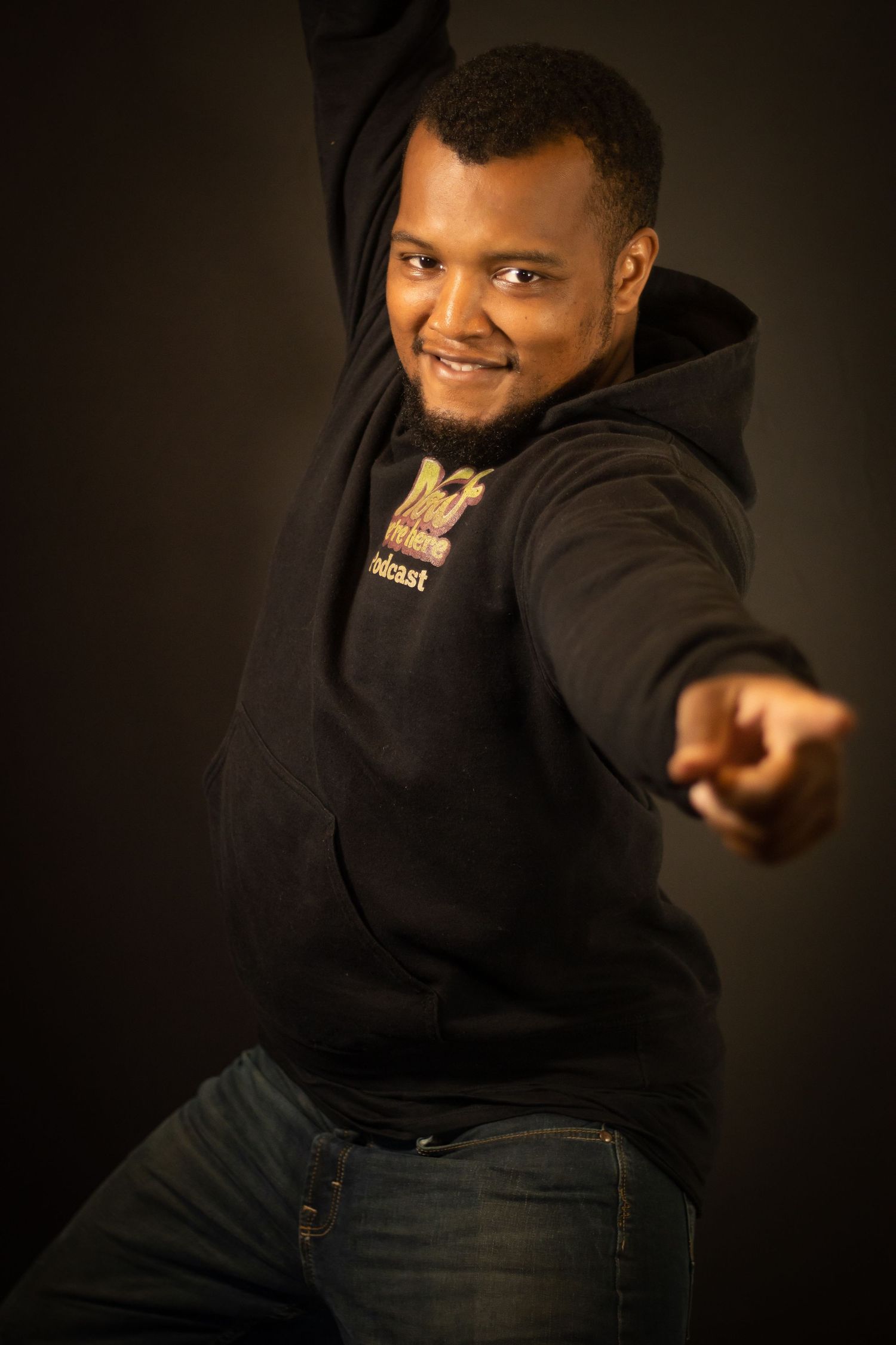 Dynamic studio portrait of a person in a black hoodie striking an energetic dance pose.