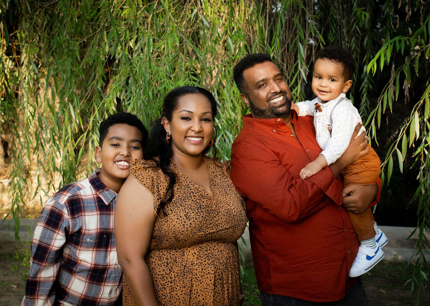 Happy family of four posing together for portrait with lush greenery background.