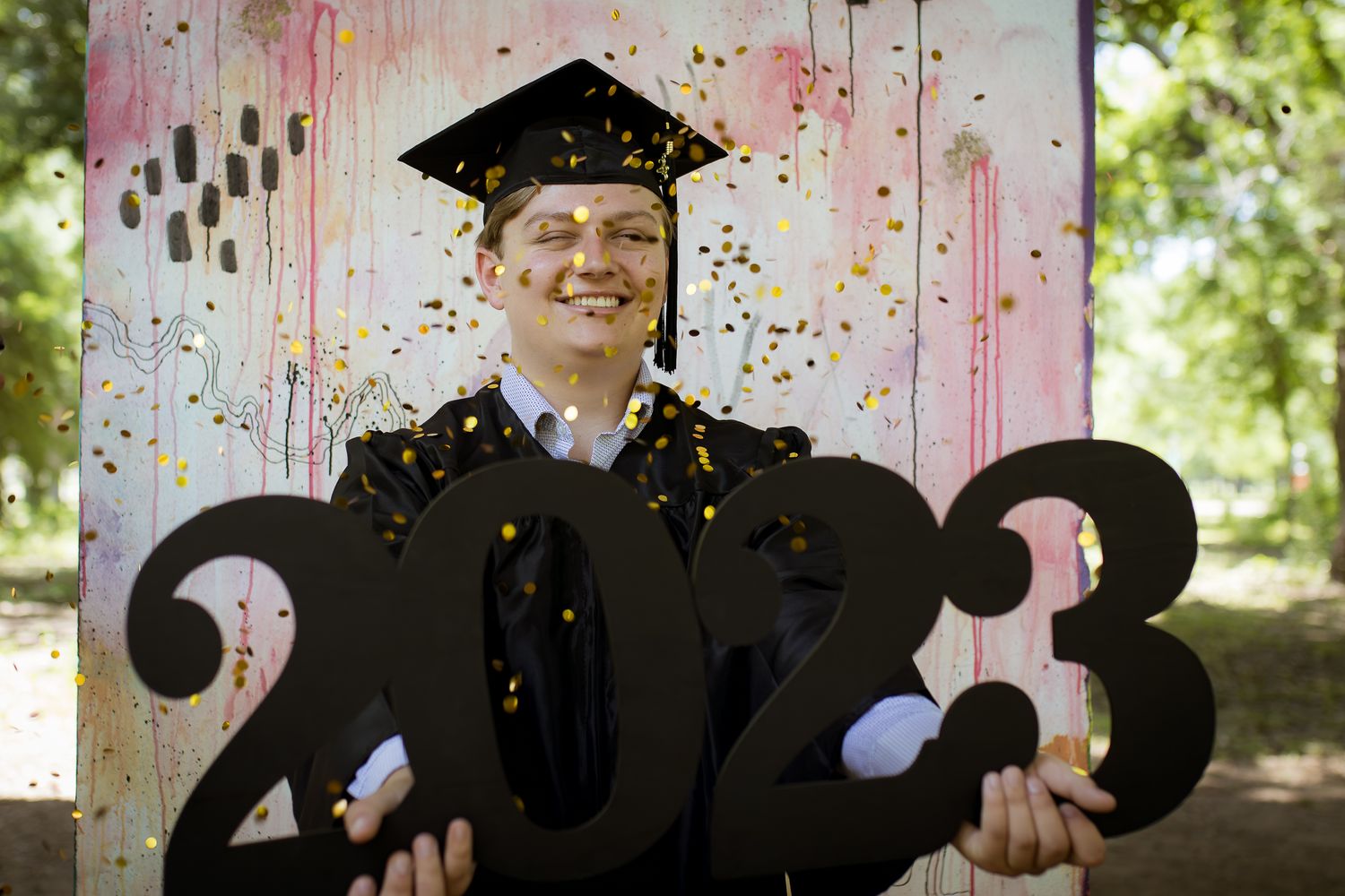A graduate poses with a 2023 sign while confetti falls in the background.