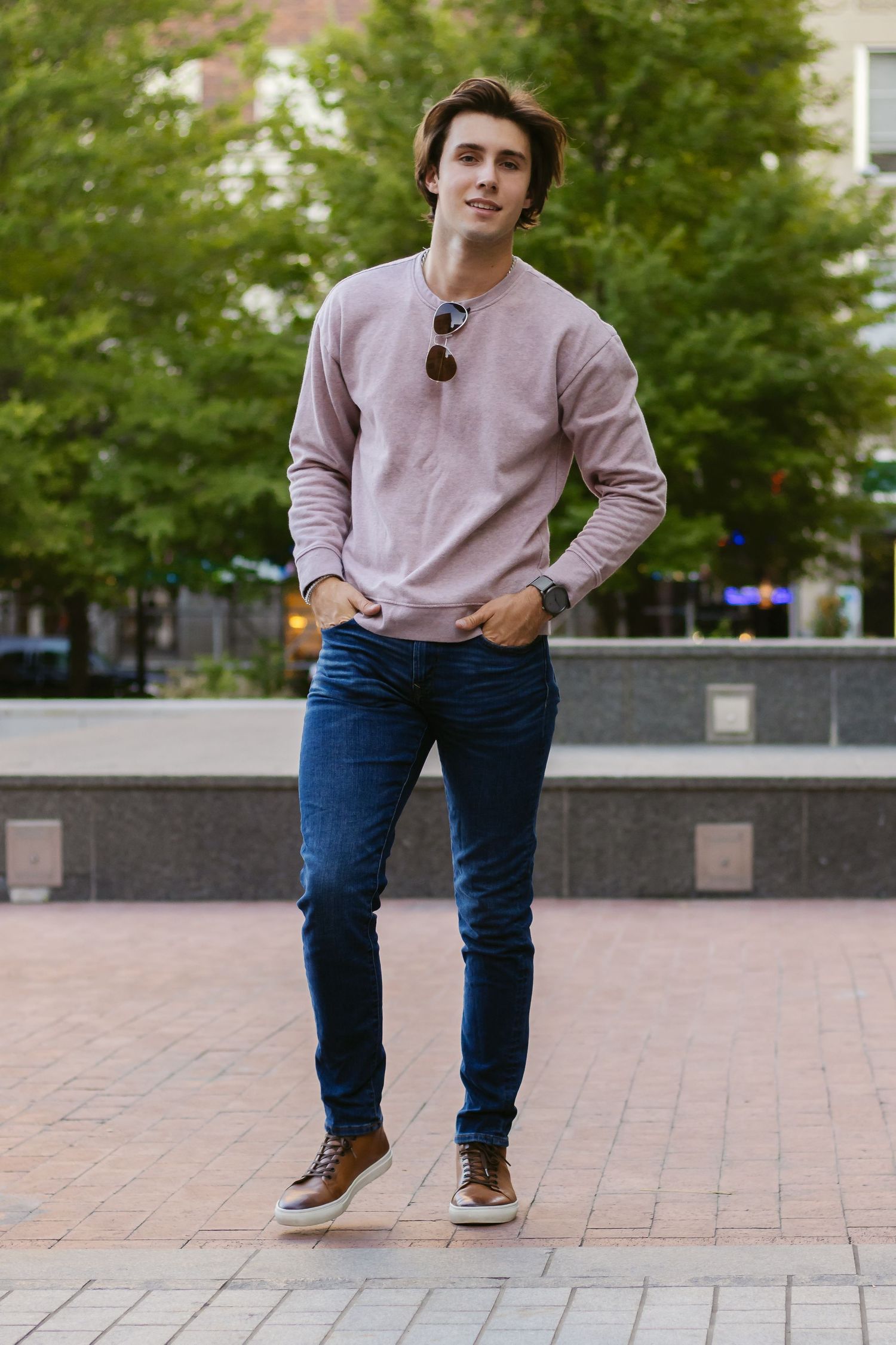 Casual street style photo of person in pink sweater and jeans standing on brick pavement.