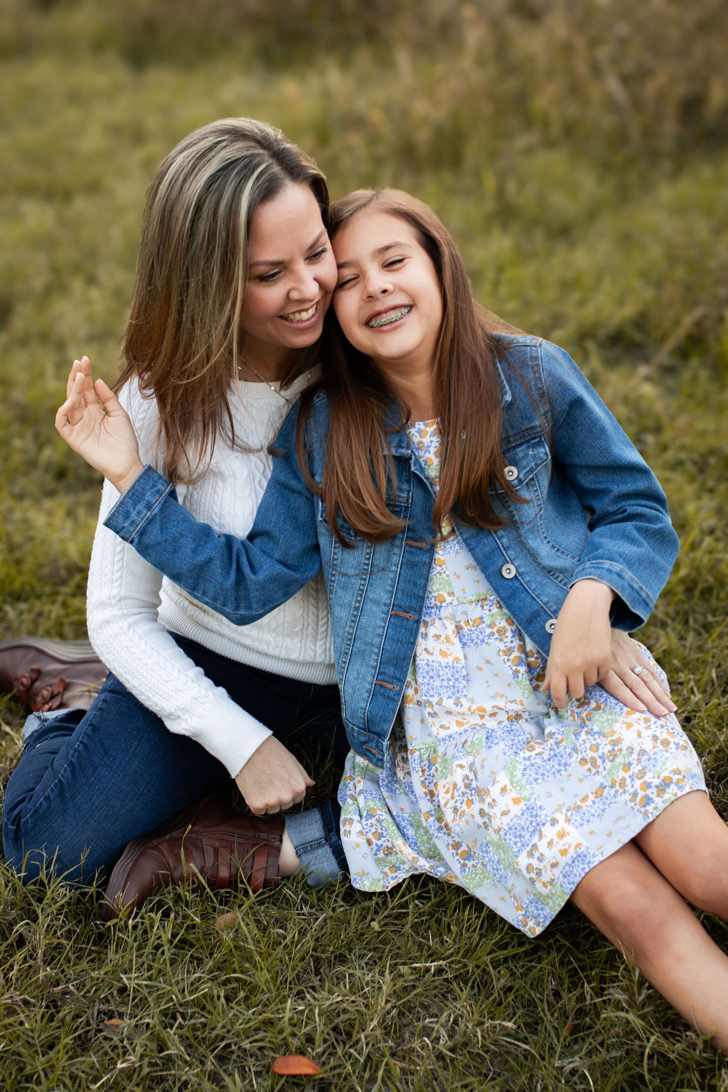 Two people share an intimate moment of laughter while sitting together on grass.