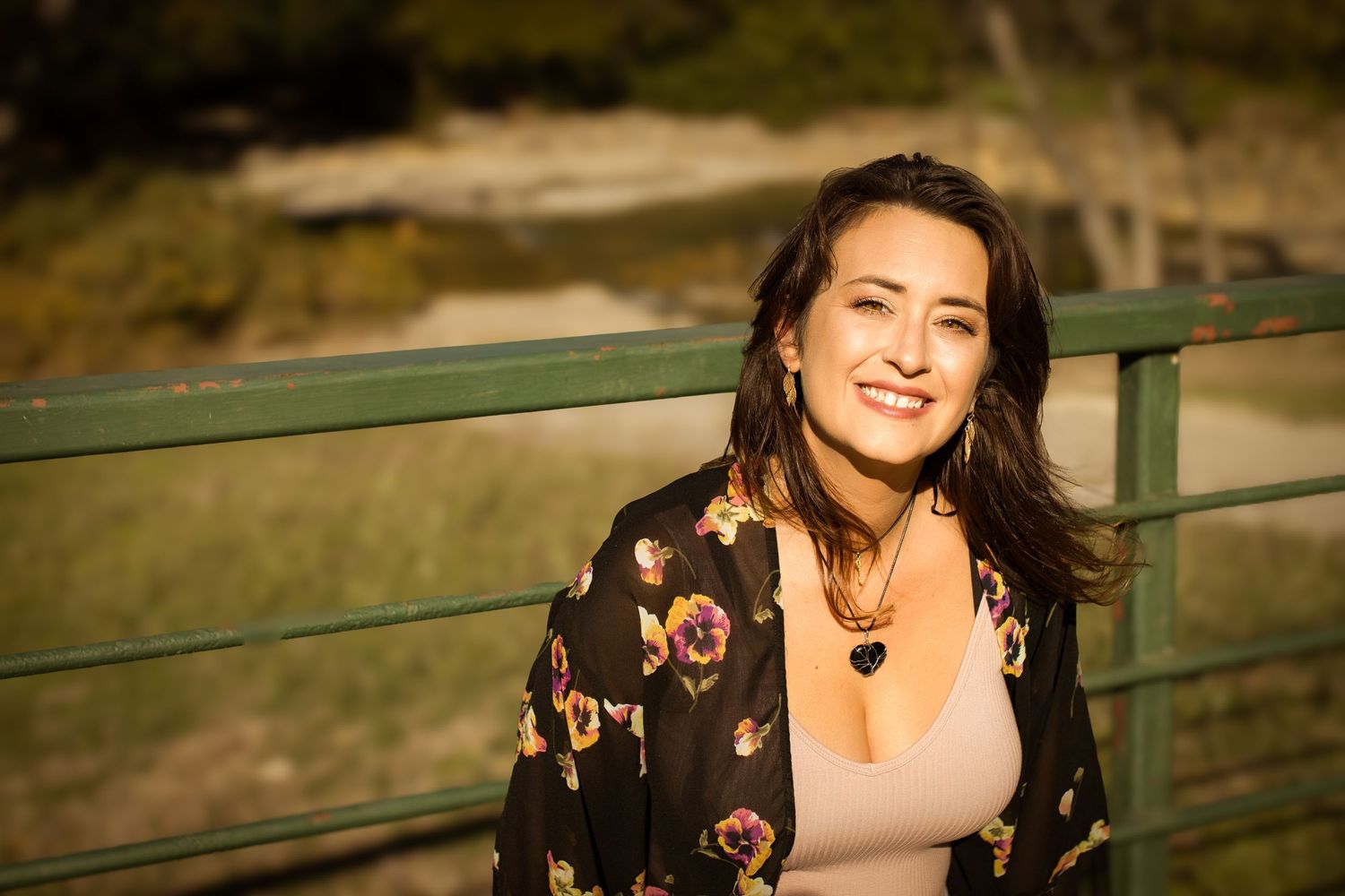 Portrait of someone in a floral cardigan and pink top posed against a railing in warm sunset lighting.