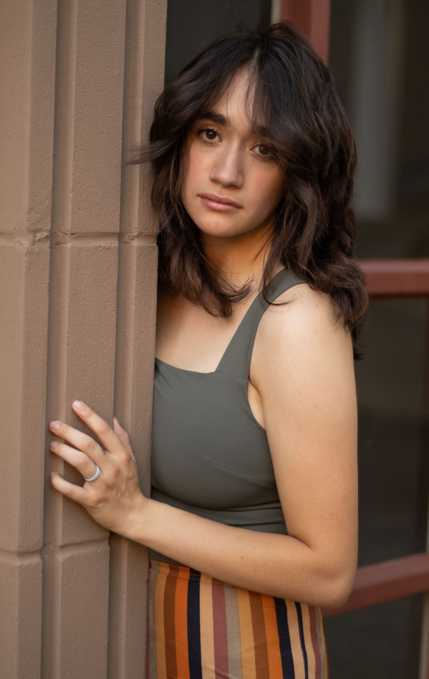 Portrait of woman in tank top leaning against wall with textured brown hair.