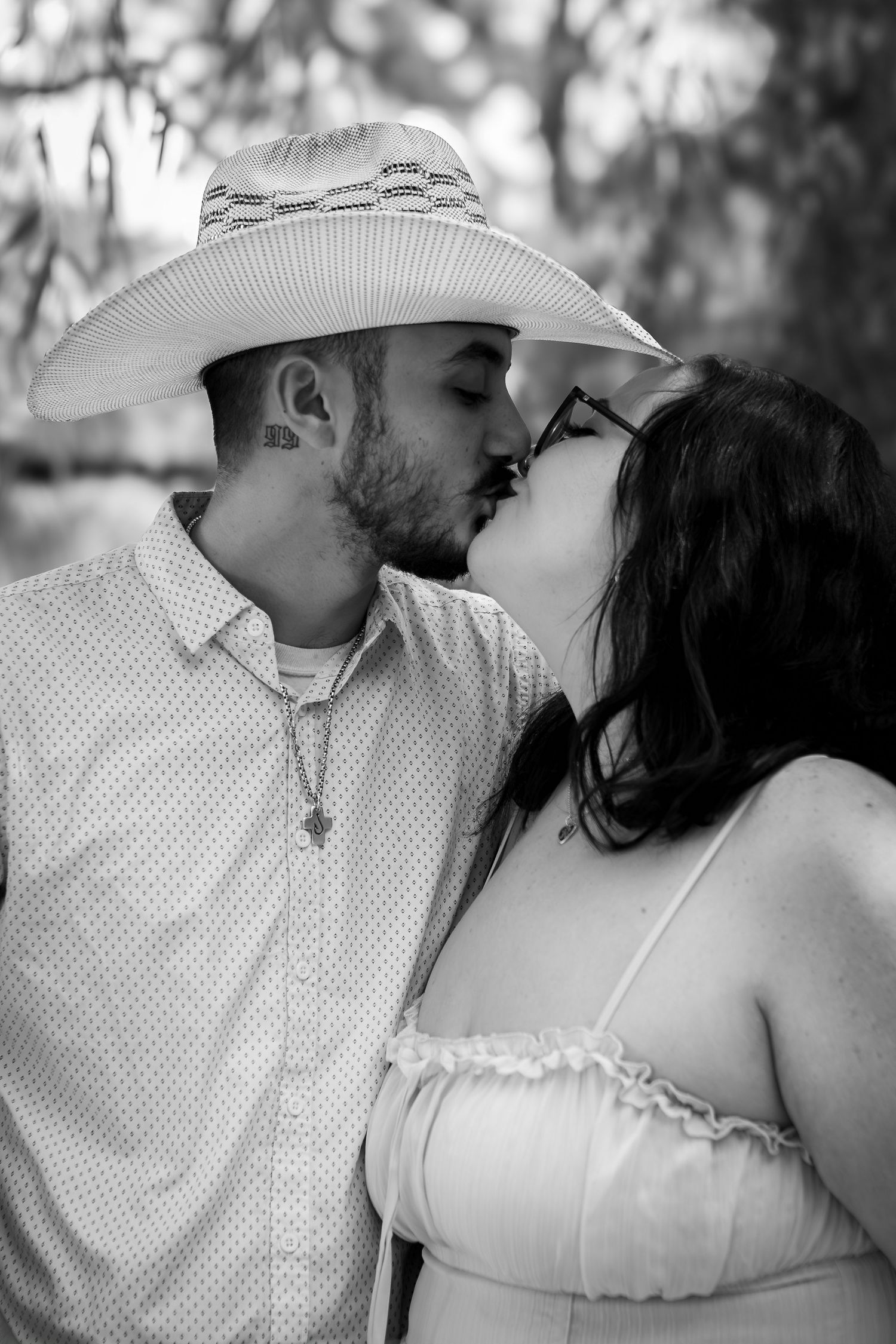 A romantic black and white portrait of a couple sharing a tender kiss under a wide-brimmed hat.