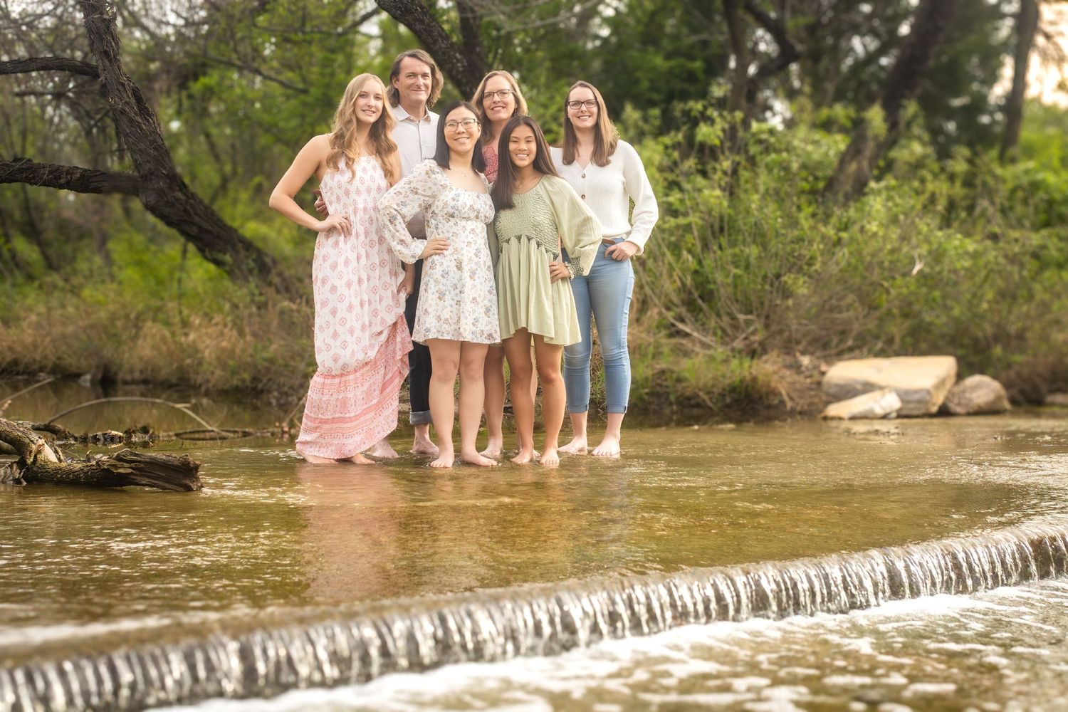 Five people in coordinated light-colored outfits stand together on a rocky ledge above a flowing waterfall during Fort Worth family photos.