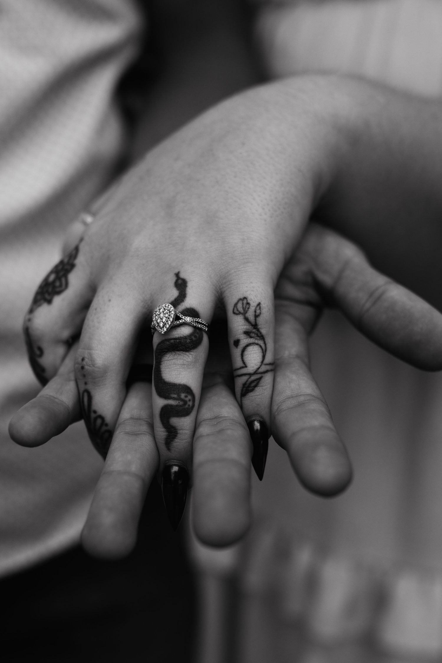 Close-up black and white photo of a hand with decorative snake and nature-themed finger tattoos.