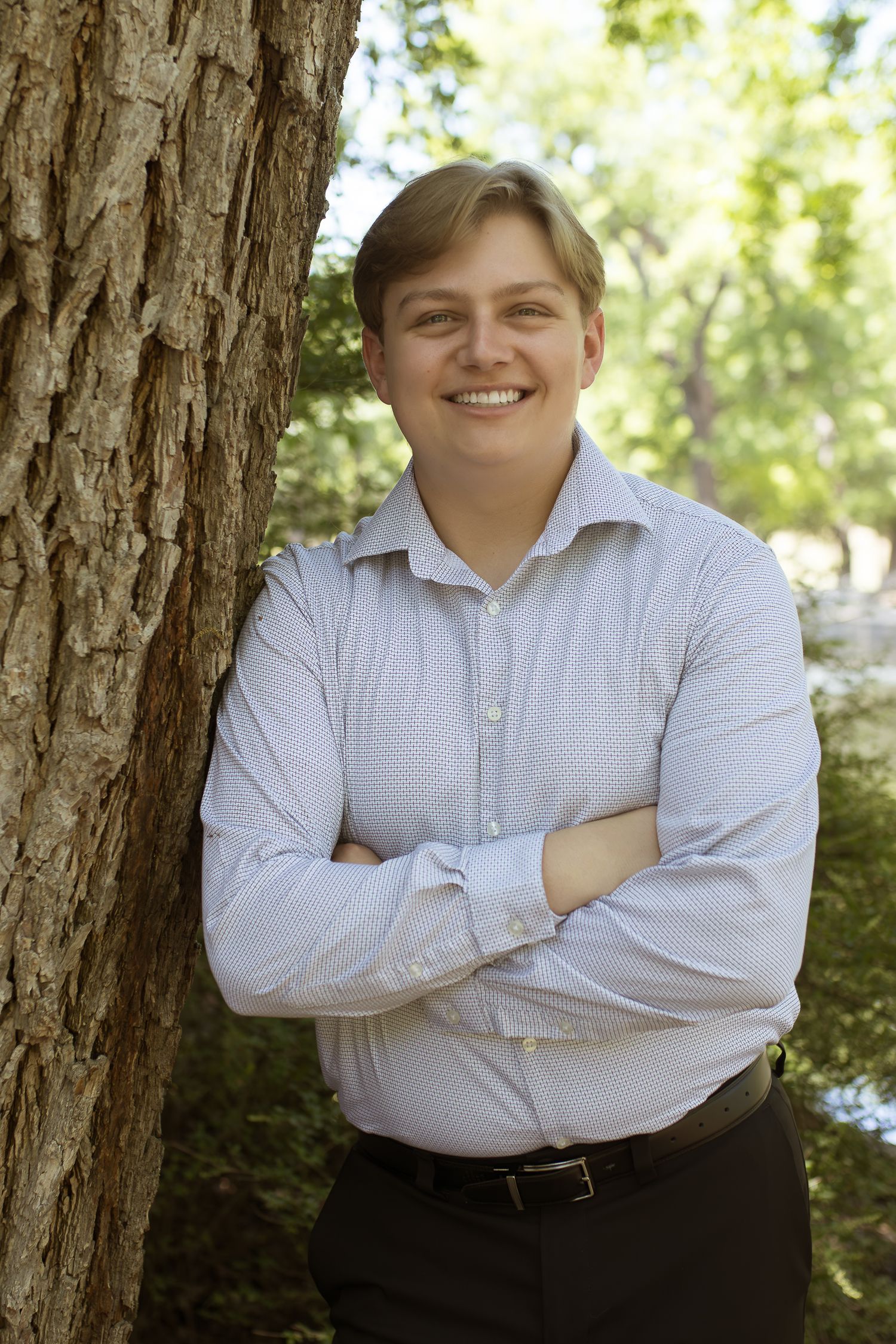 Outdoor portrait of person in striped shirt leaning against tree trunk.