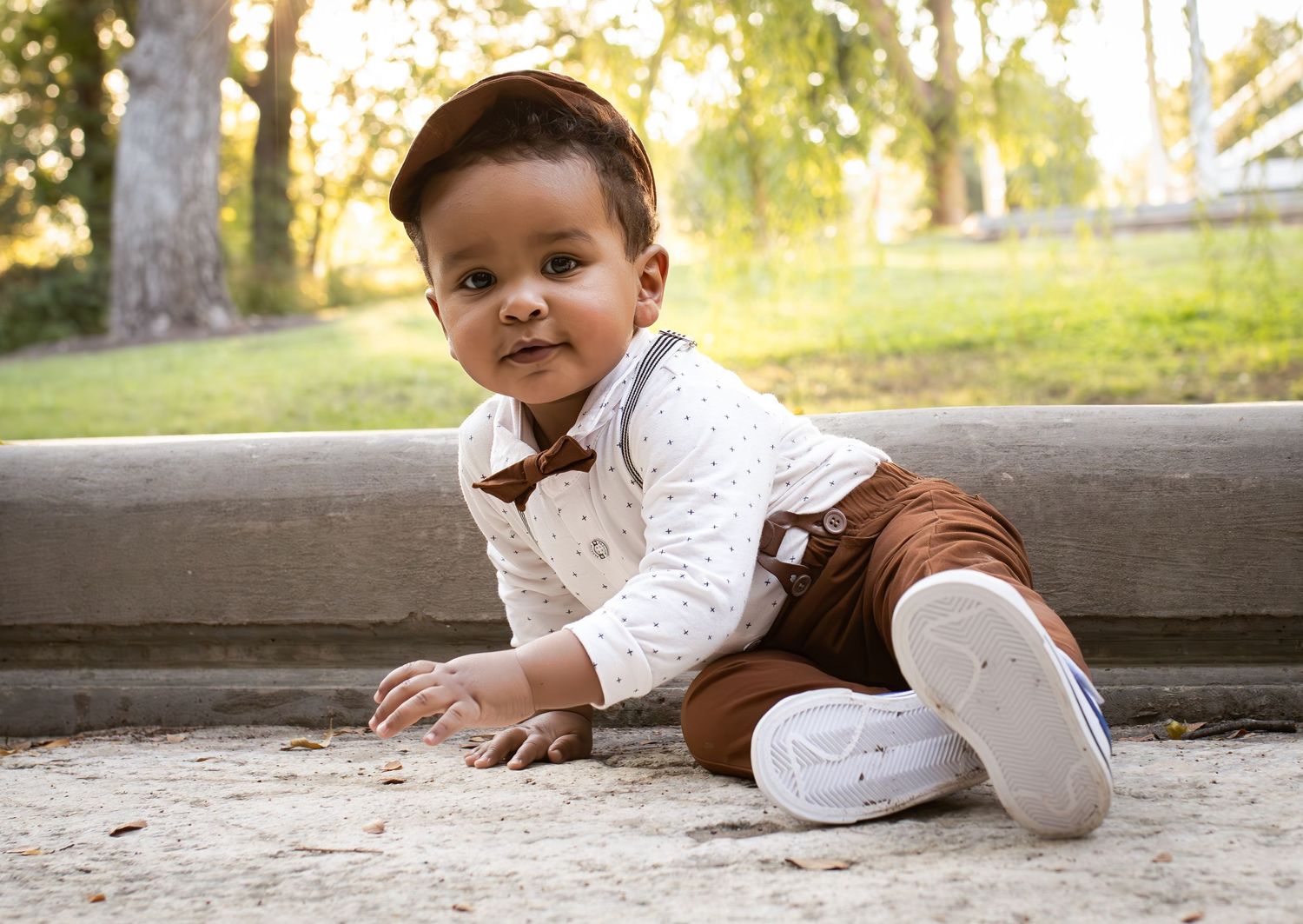 Toddler in white shirt and brown pants sitting on concrete surface outdoors.