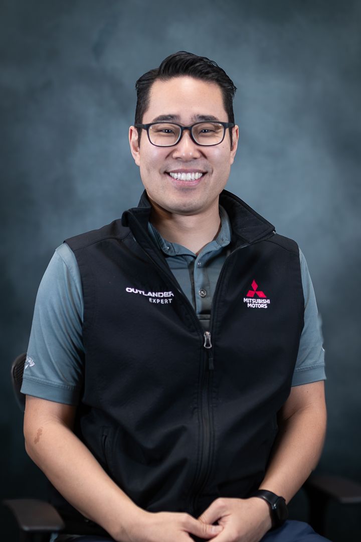 Professional headshot of employee wearing glasses and black vest with company logo.