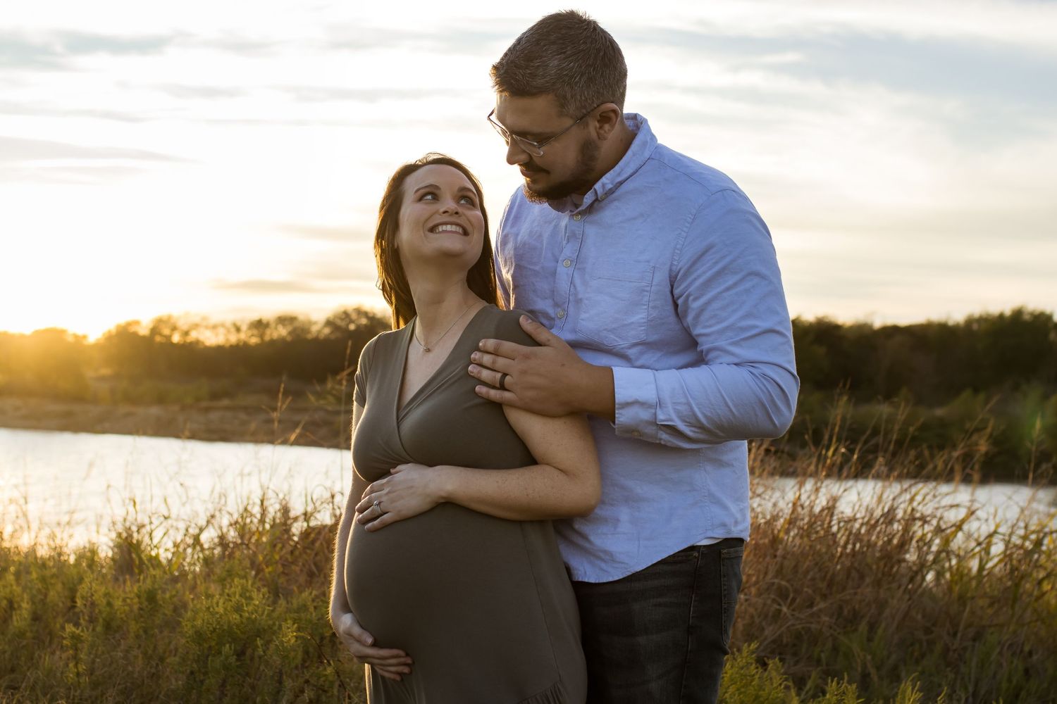 Expectant couple shares tender moment by lakeside at sunset during golden hour maternity photoshoot in Grapevine, TX.