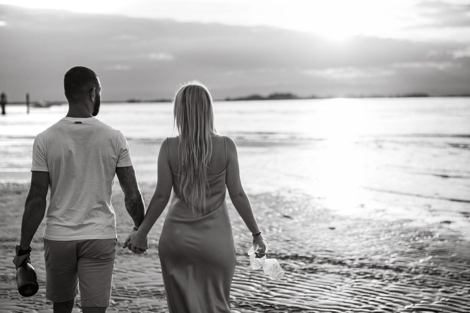 Silhouetted couple walking hand in hand along beach at sunset.