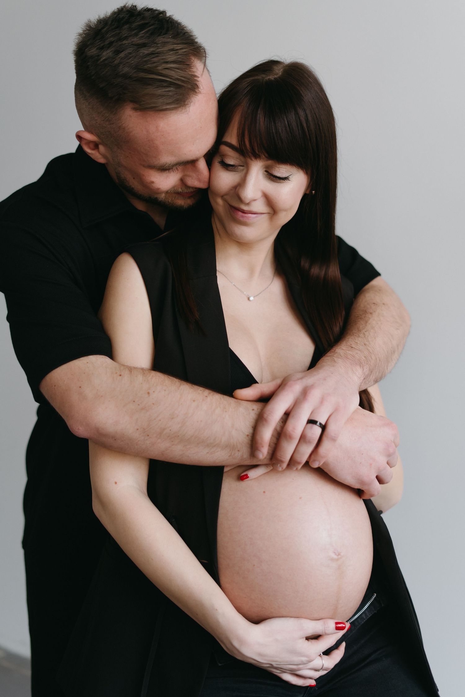 Tender embrace captured in black and white maternity photo against minimal background.