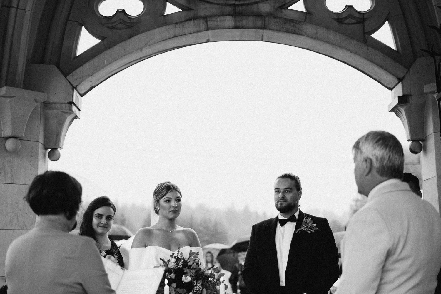 Black and white photo of a wedding ceremony taking place under an ornate stone archway.