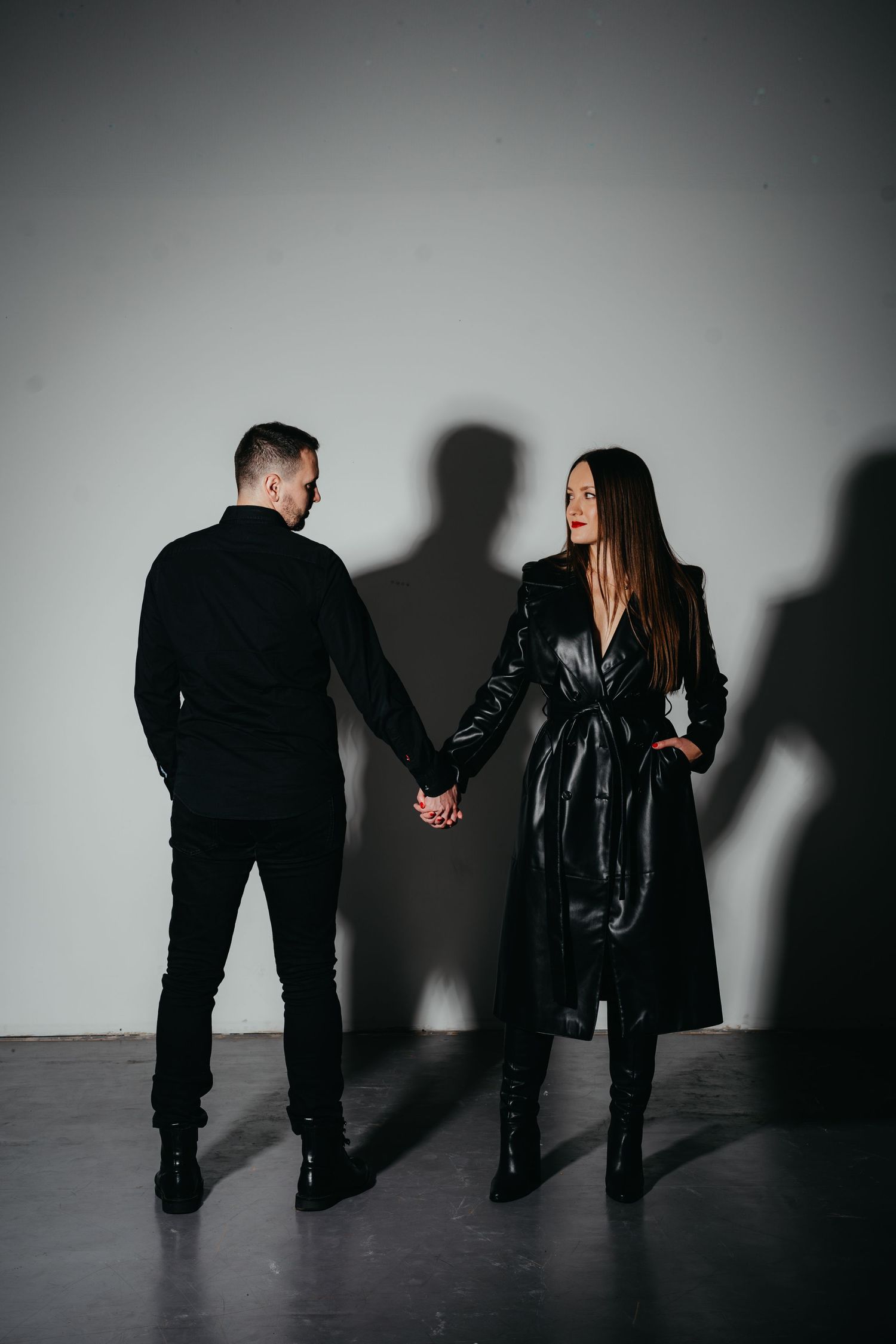 Dramatic shadow play portrait of couple holding hands against grey wall.