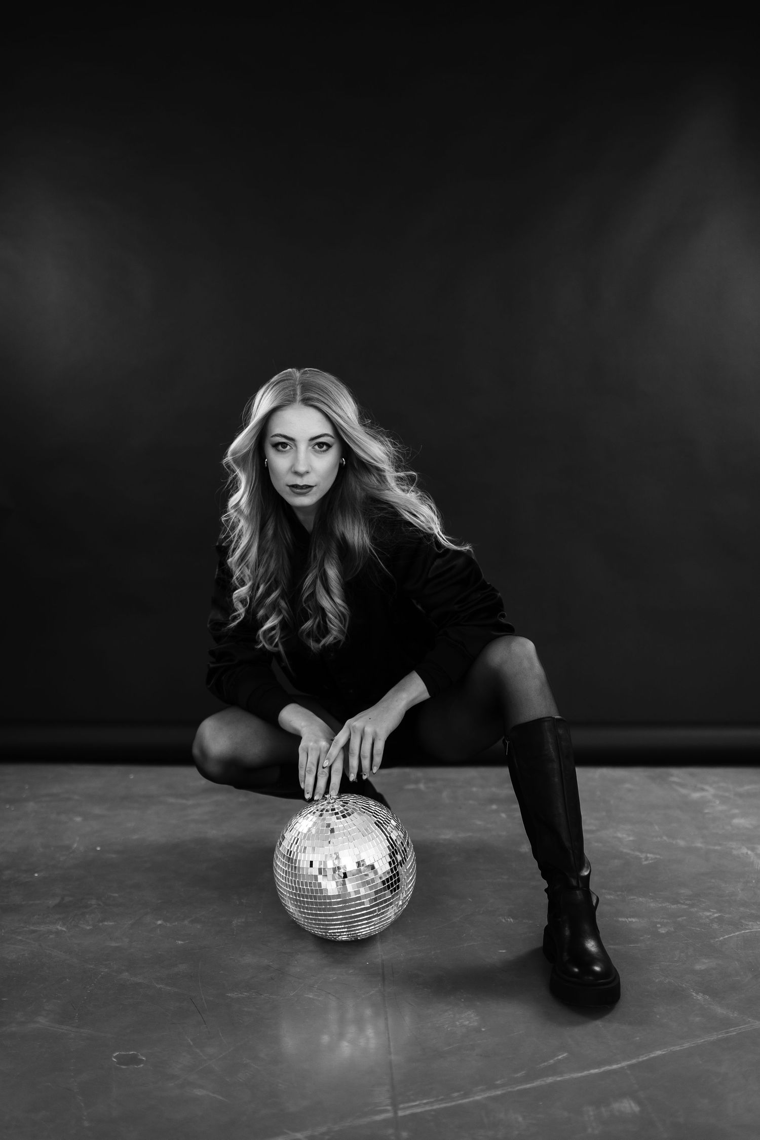 Black and white photo of a blonde woman in black outfit posing with a disco ball on the floor.