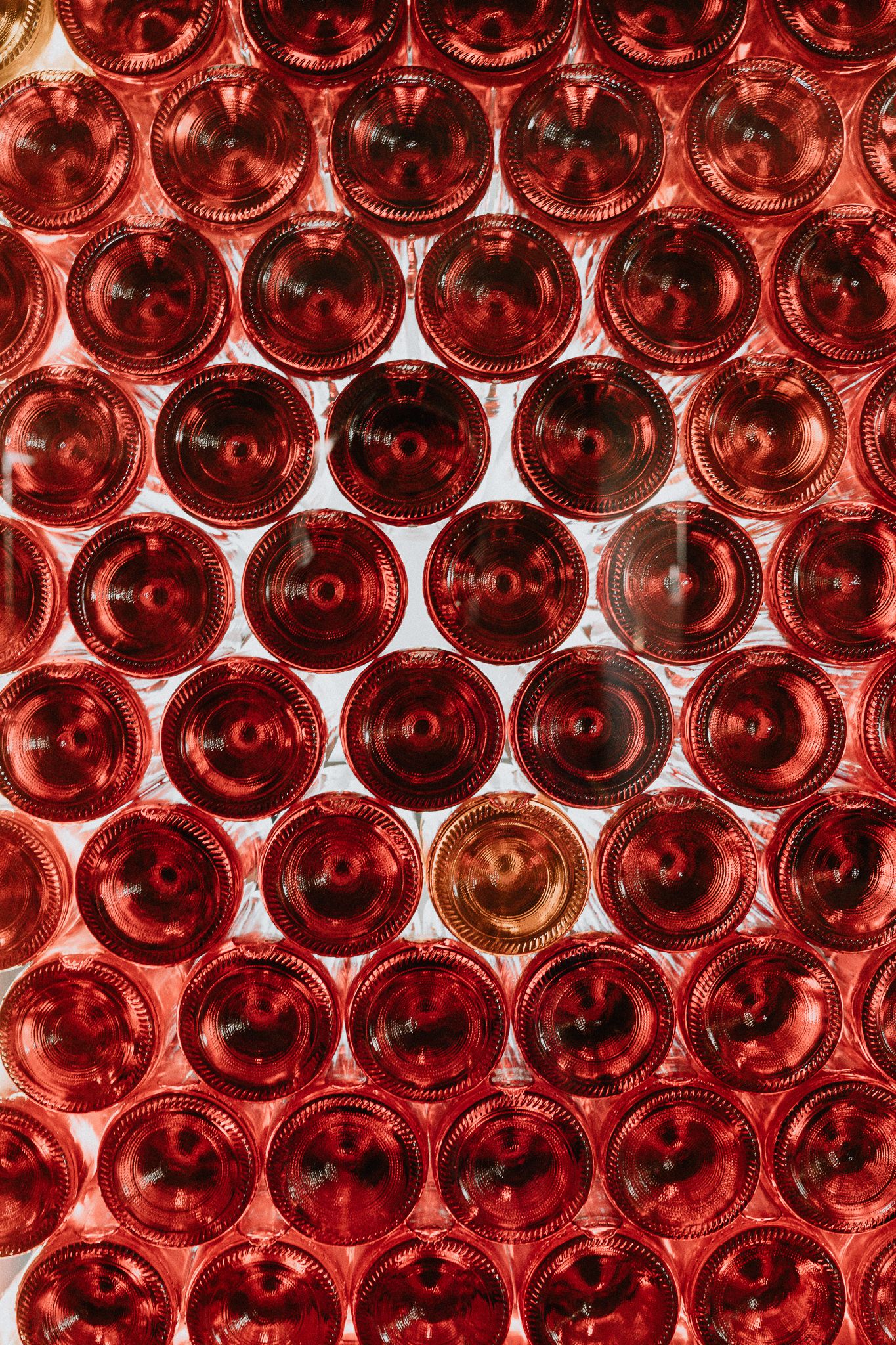 Close-up pattern of red glass wine bottles arranged in rows, creating a repetitive circular design and rich burgundy color.