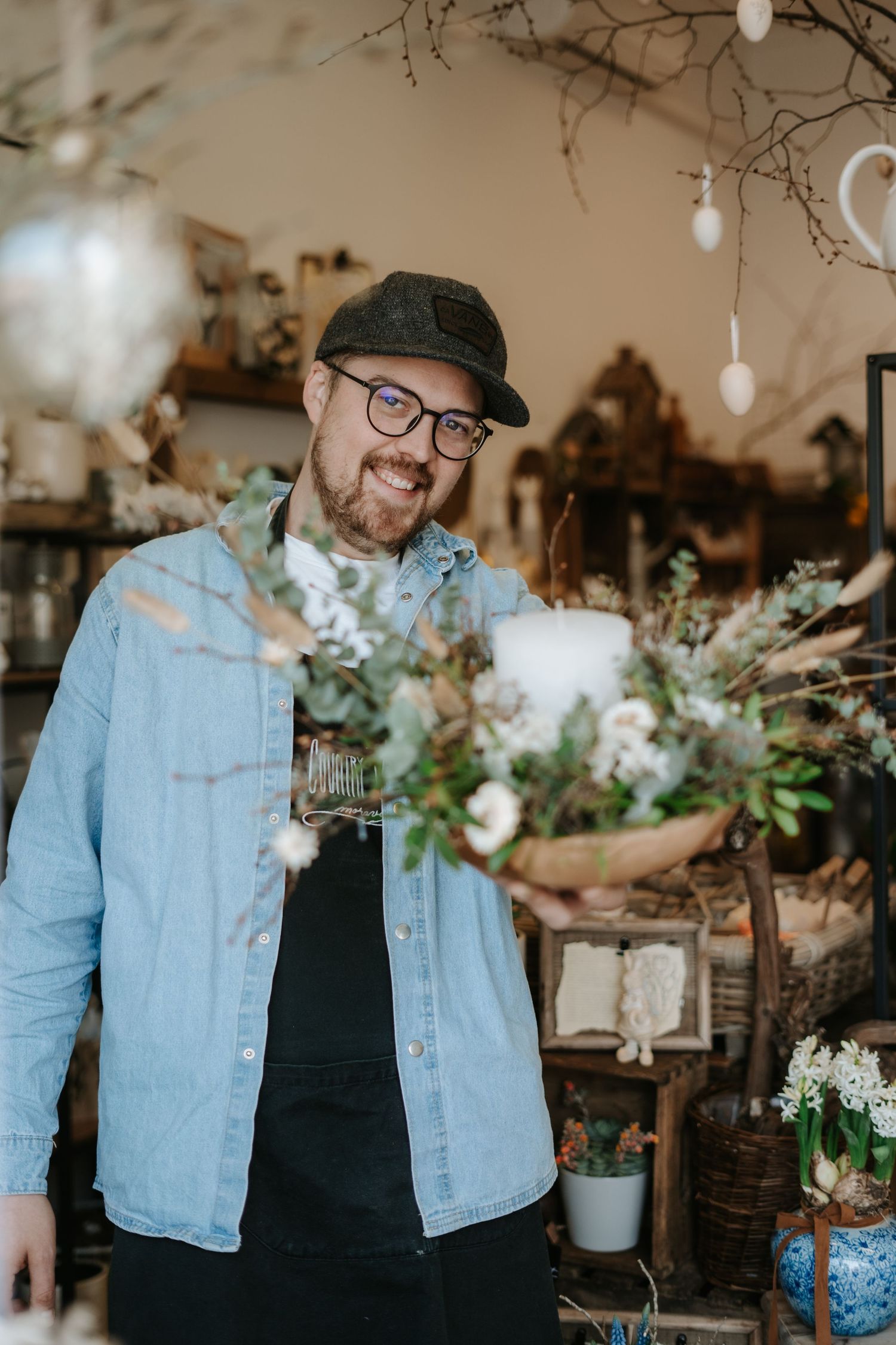 Inside a cozy floral shop, someone works among arrangements of dried flowers and string lights.
