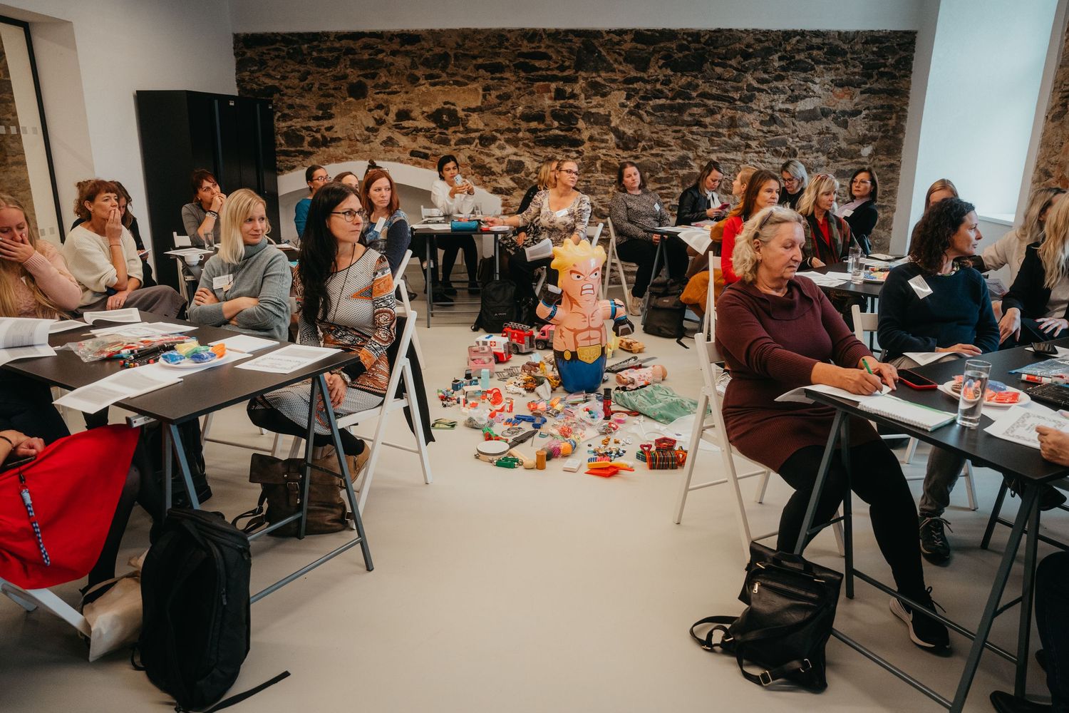 Workshop participants collaborate at tables in a stone-walled meeting space while engaging in group activities.
