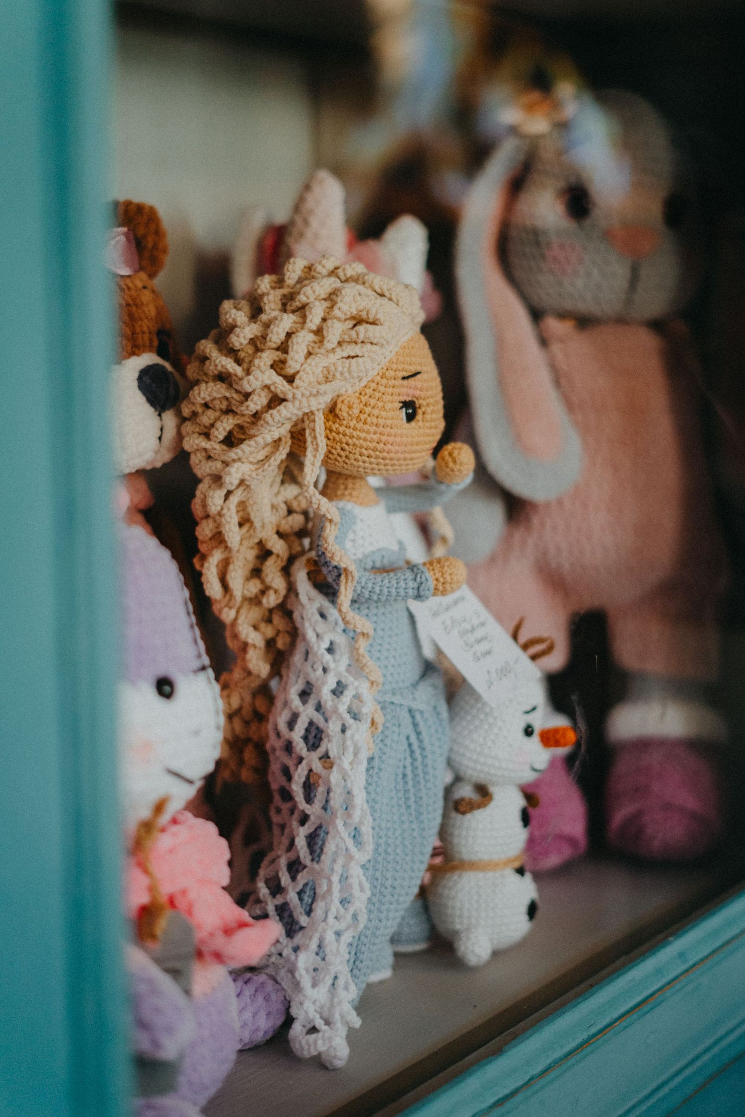 Handmade crochet dolls with curly yarn hair displayed on turquoise painted wooden shelving.