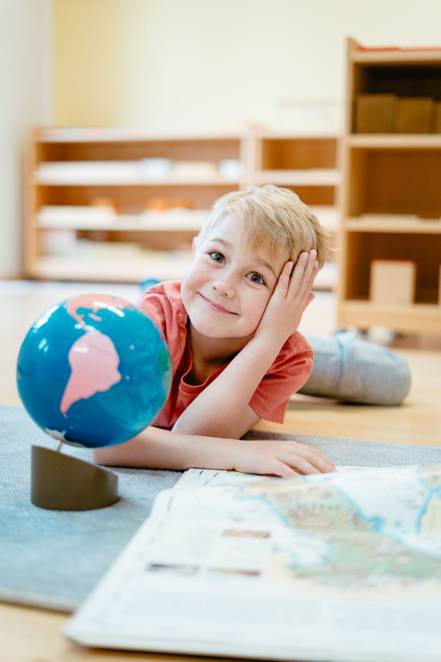 A child lies on the floor looking at papers and learning materials with a blue balloon visible in the frame.