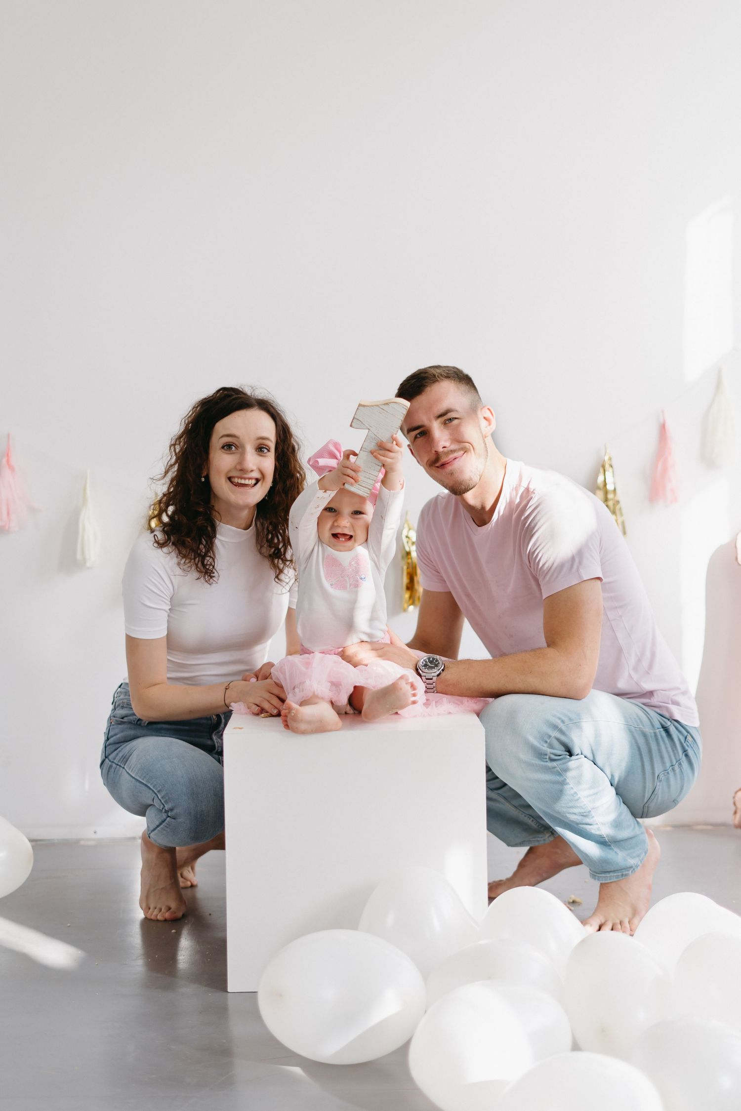 Family sitting together on a white platform surrounded by balloons in a minimalist setting.