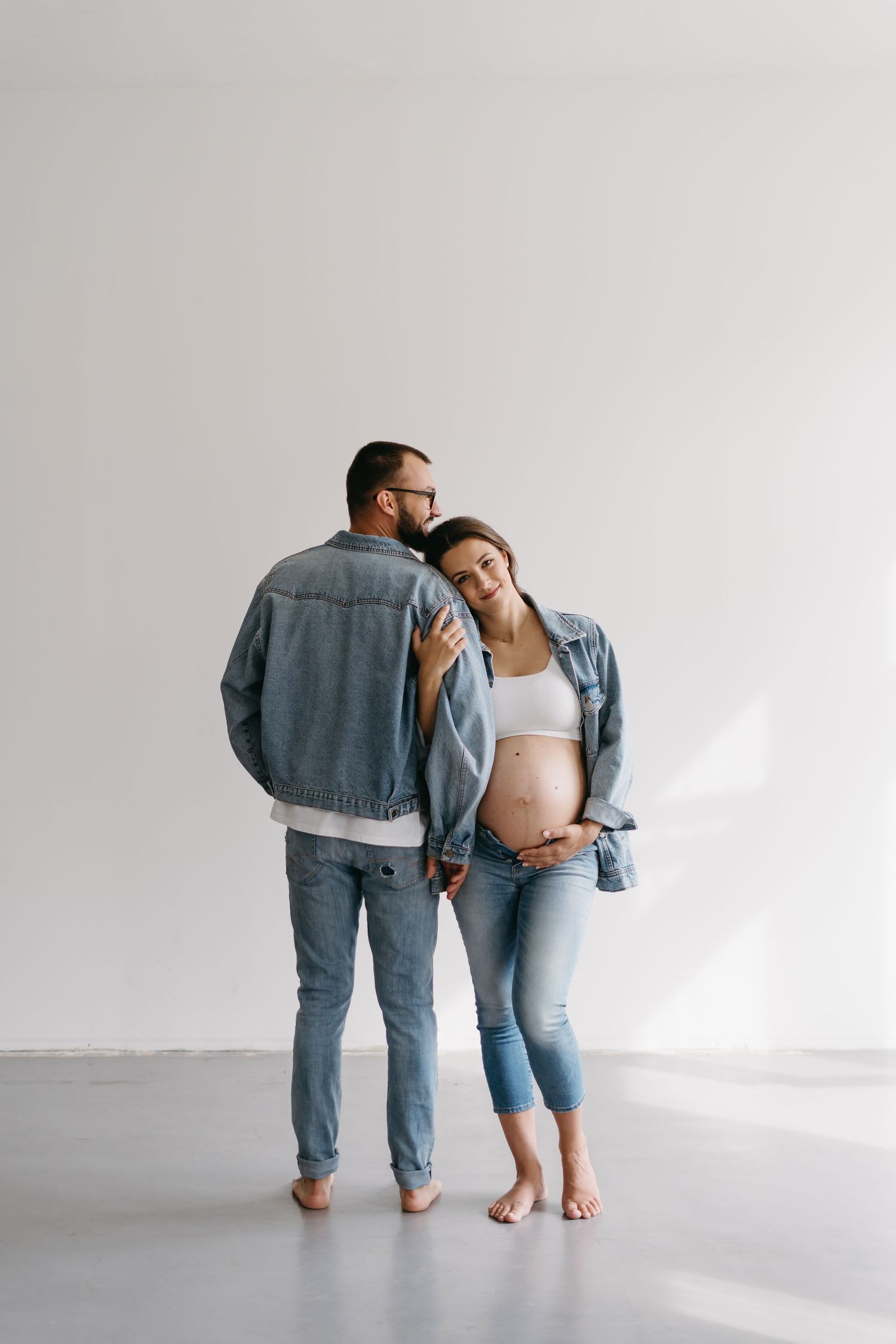 Couple in matching denim outfits shares playful moments during indoor maternity shoot.