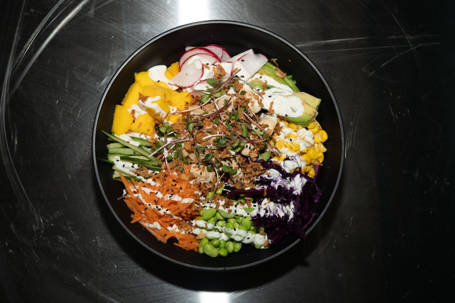Colorful poke bowl with fresh fish, vegetables, and seaweed on black plate against dark background.