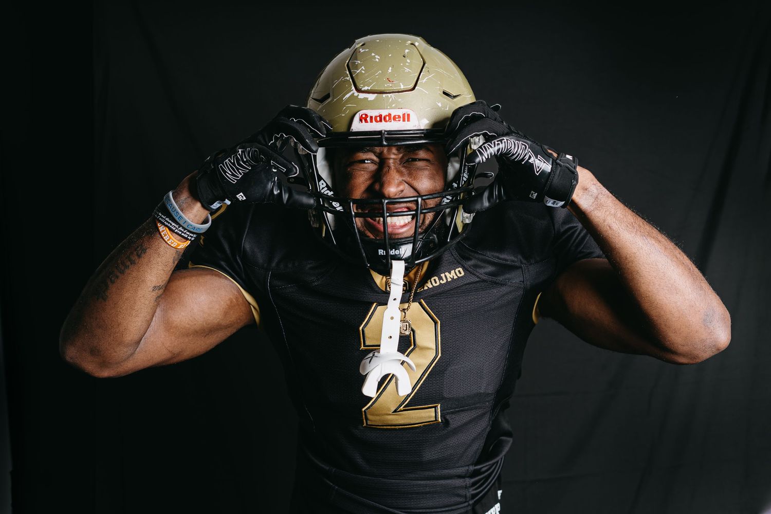 Football player wearing black jersey with number 2 and gold helmet reacts emotionally during photoshoot.