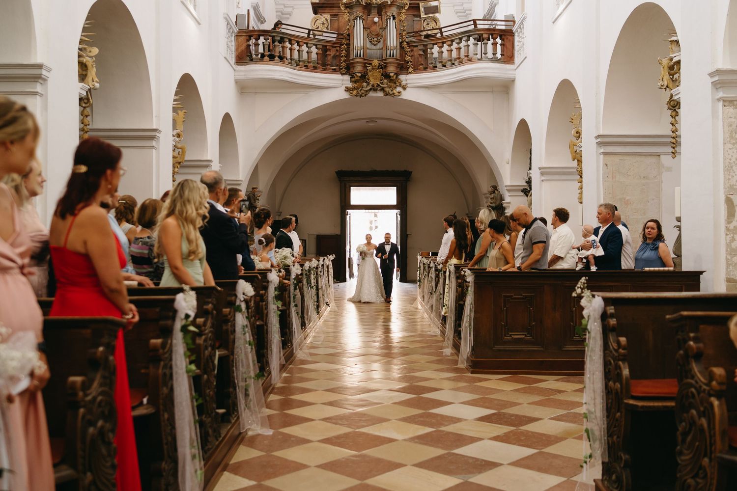 Elegant church wedding ceremony with guests seated in wooden pews along a decorated aisle leading to the altar.