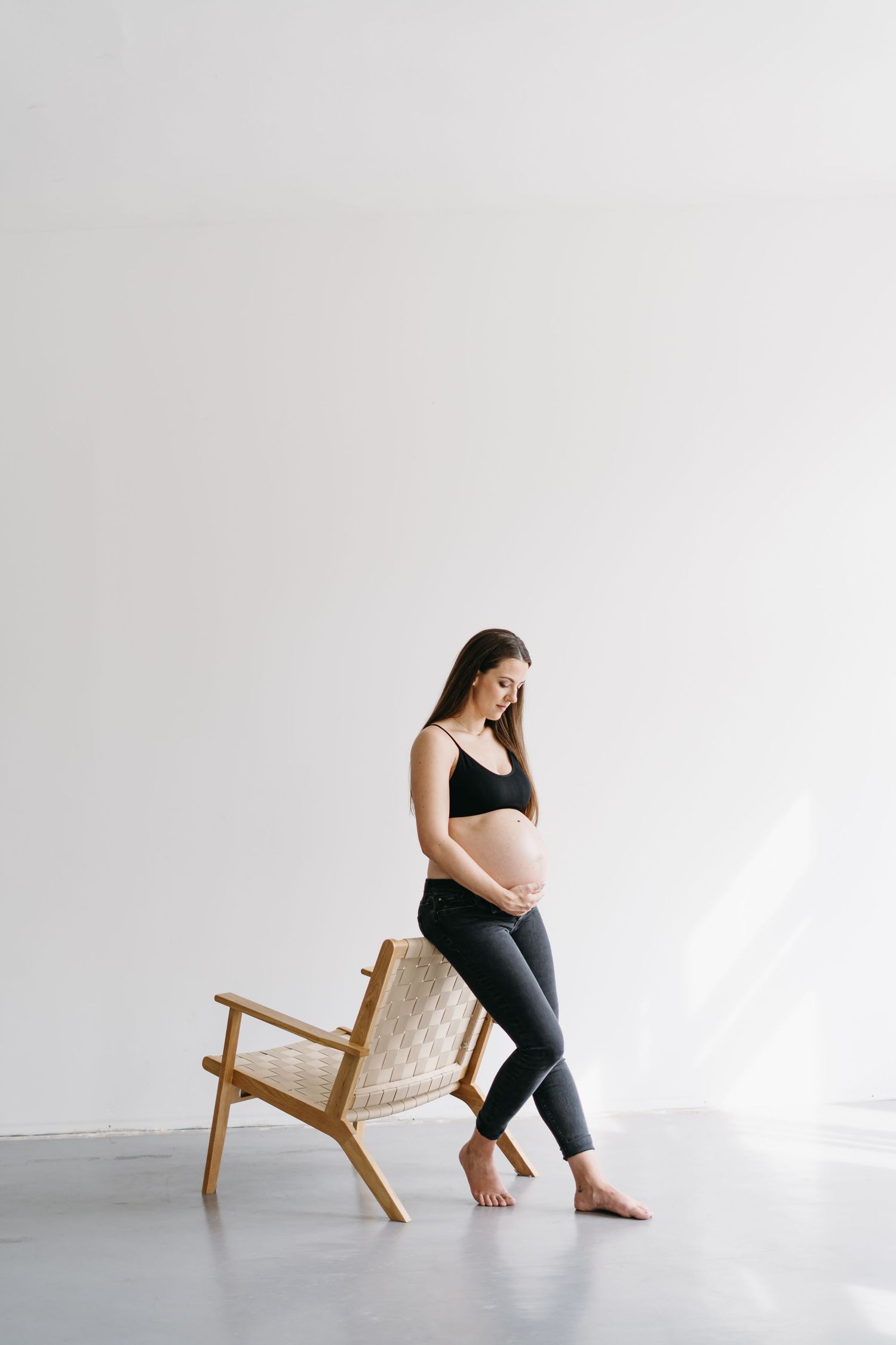 Peaceful maternity portrait with expectant mother seated on modern wooden chair.
