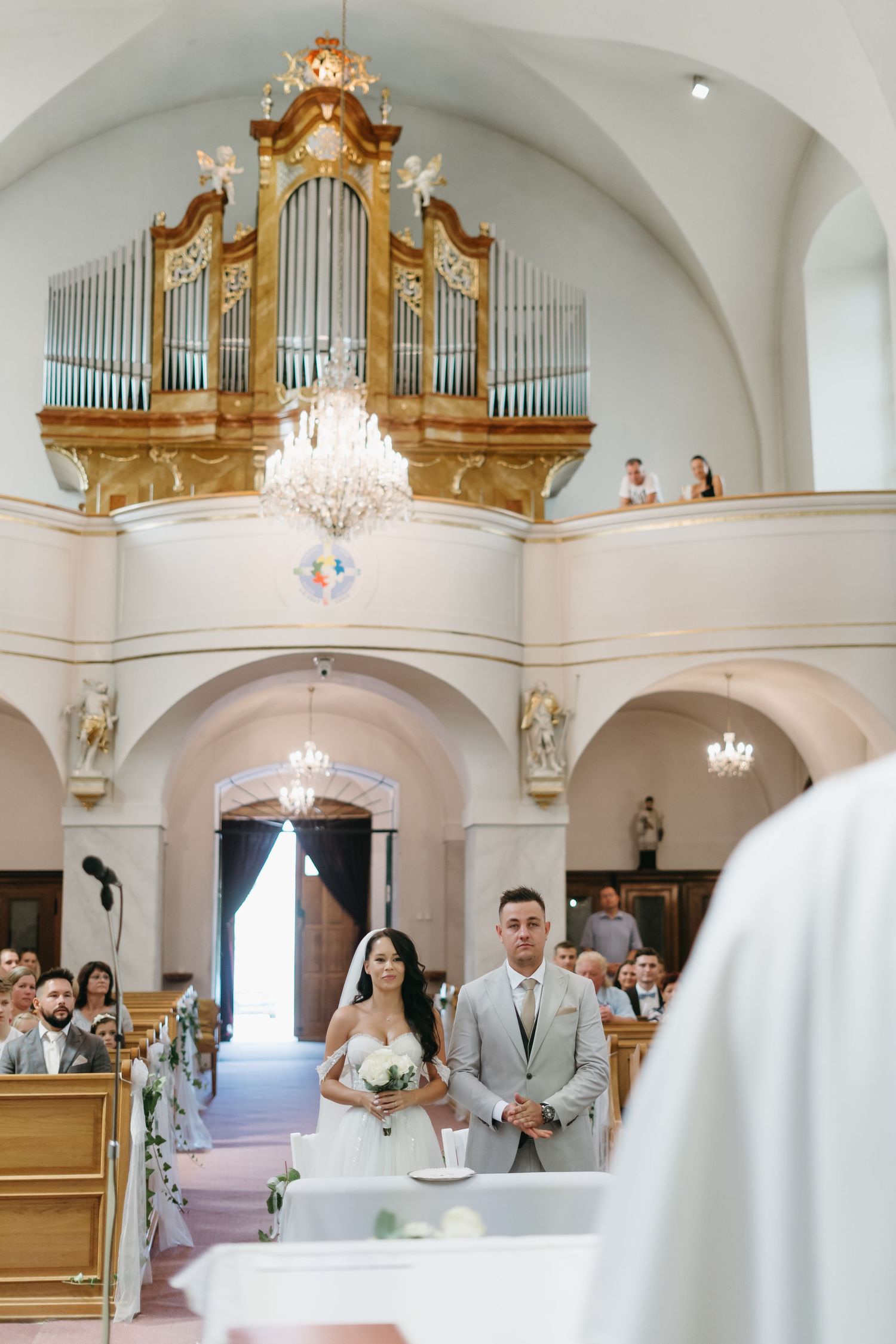 Wedding ceremony in ornate church with grand pipe organ and crystal chandelier.