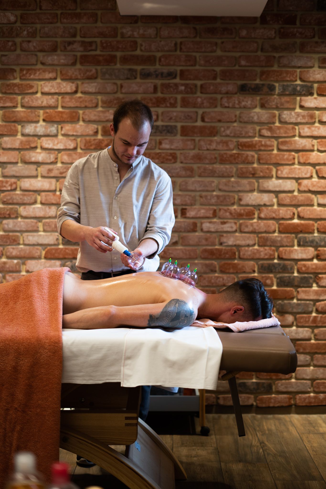Professional wellness treatment being performed on massage table against rustic brick wall interior.