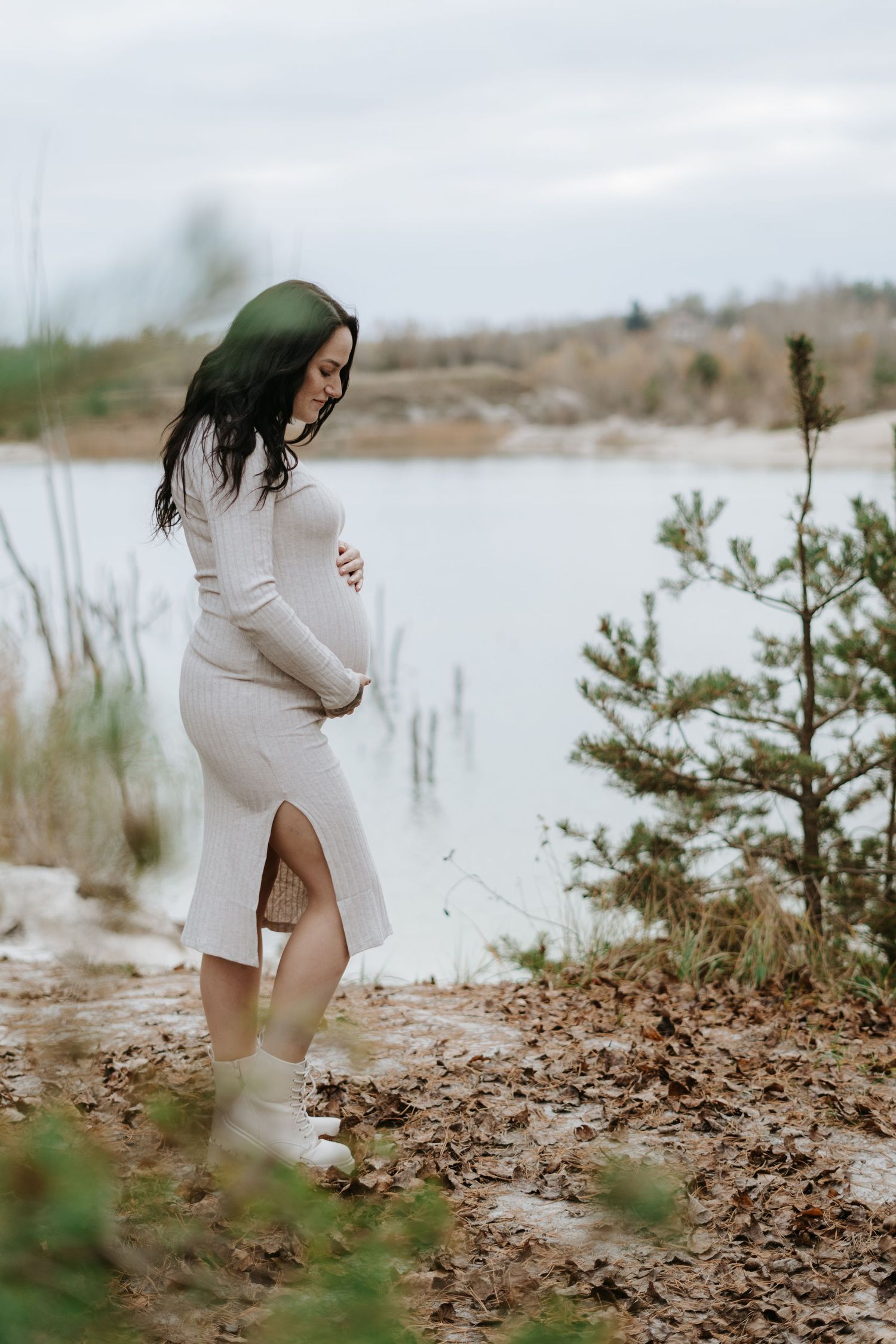 Expecting couple takes romantic maternity photos on a sandy beach near a serene lake.