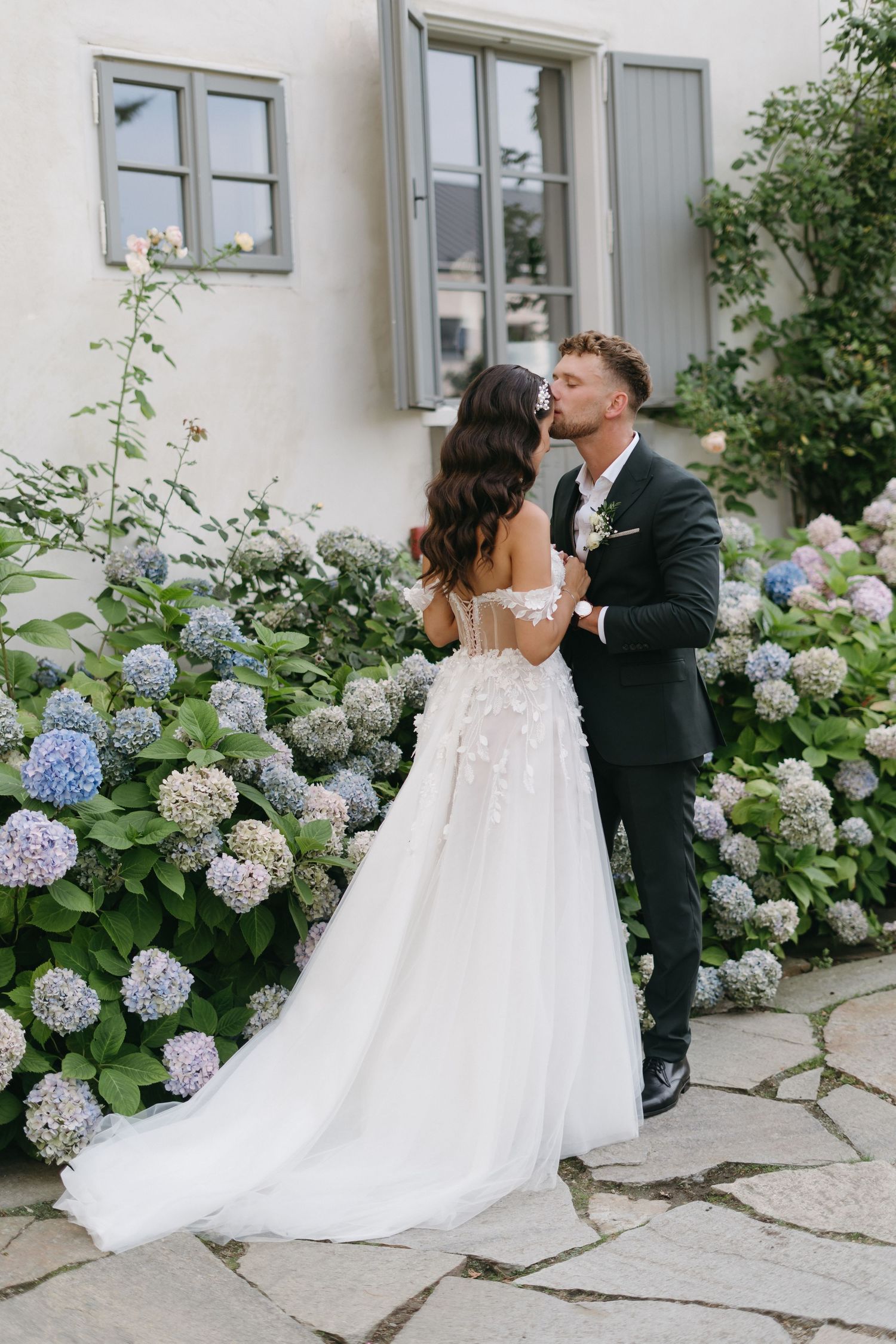 Wedding couple shares romantic moments in garden with blooming blue hydrangea flowers.