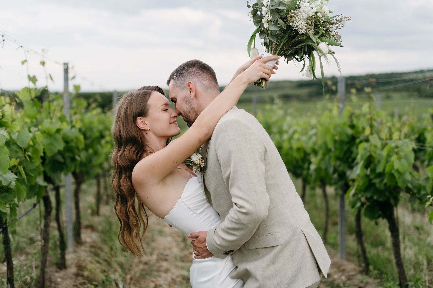 A couple embraces passionately while standing in a green vineyard on their wedding day.
