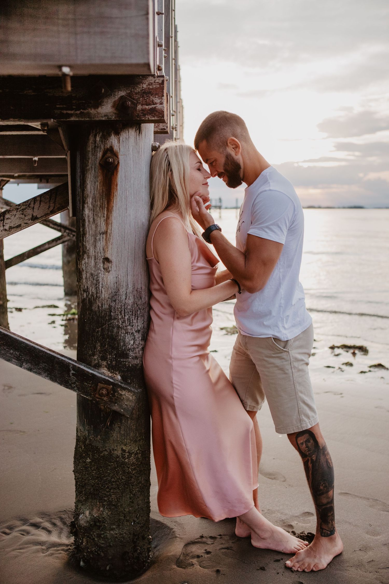 Intimate moment between couple by wooden pier during sunset.