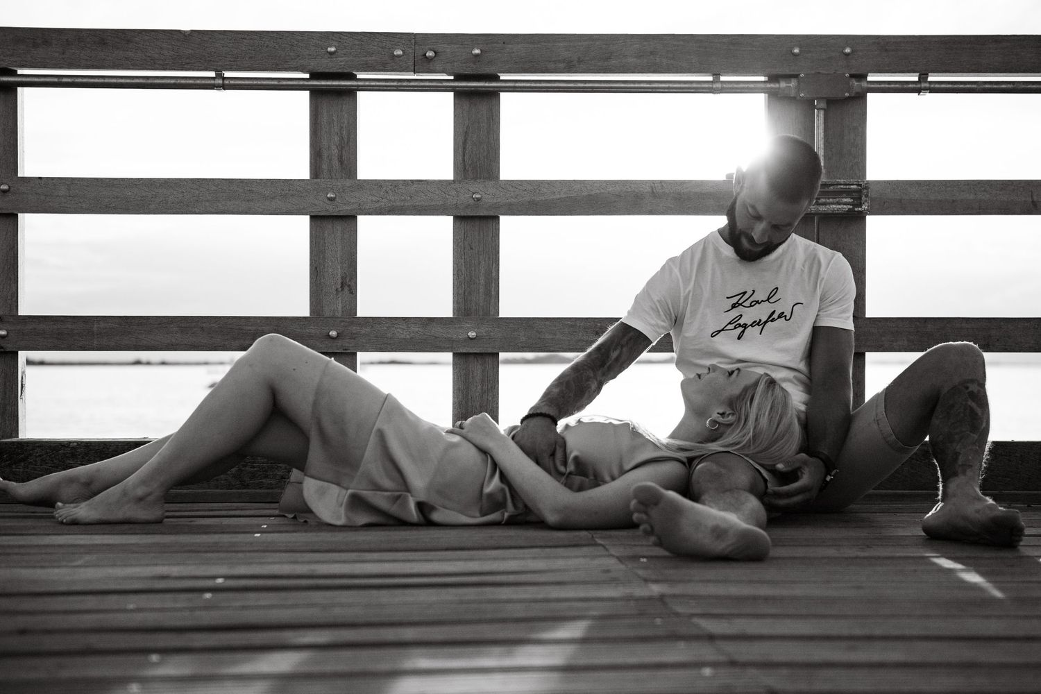 Couple relaxing together on wooden dock in black and white.