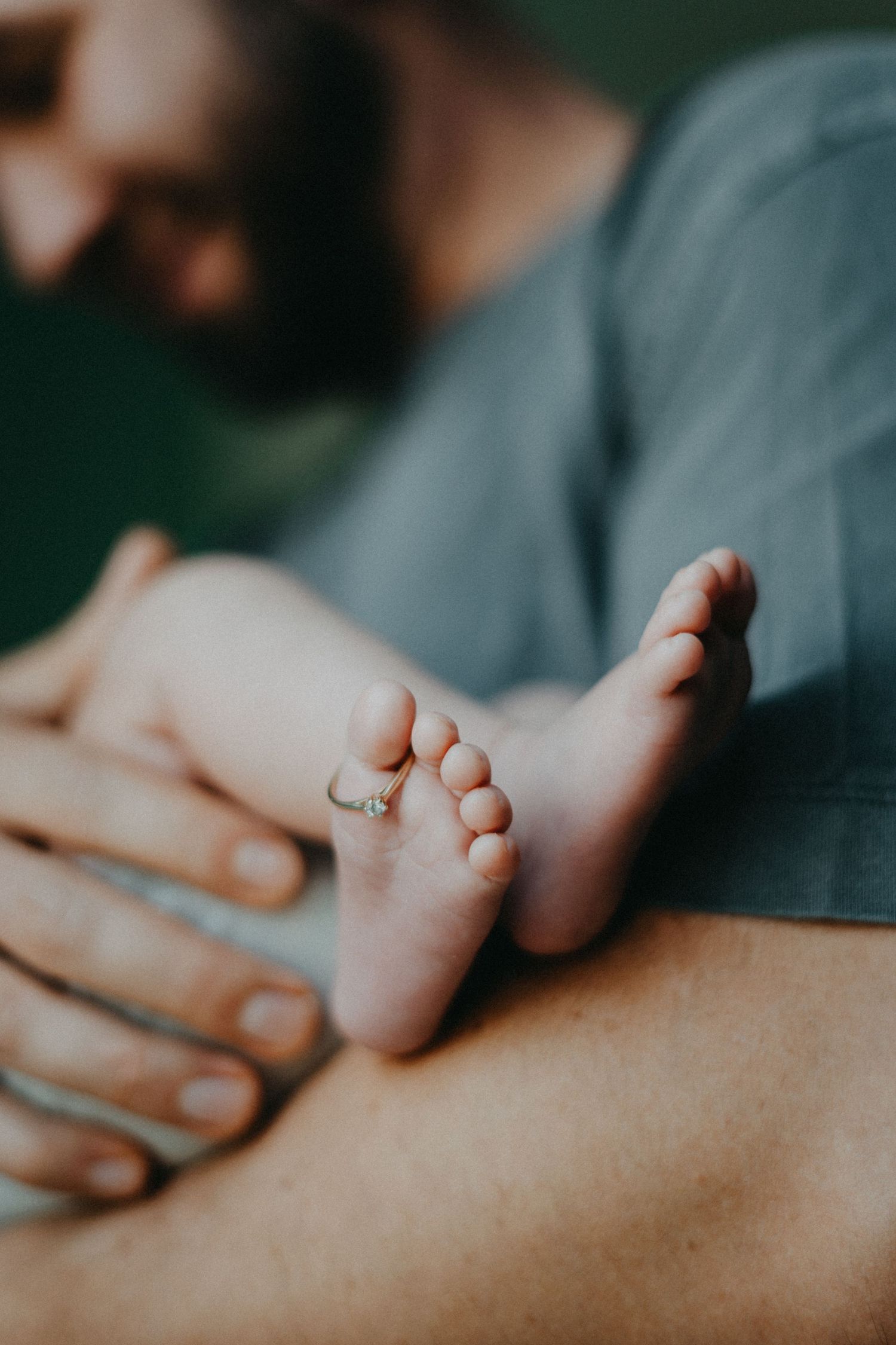 Close-up of tender moment with baby's feet being gently held against blue background.
