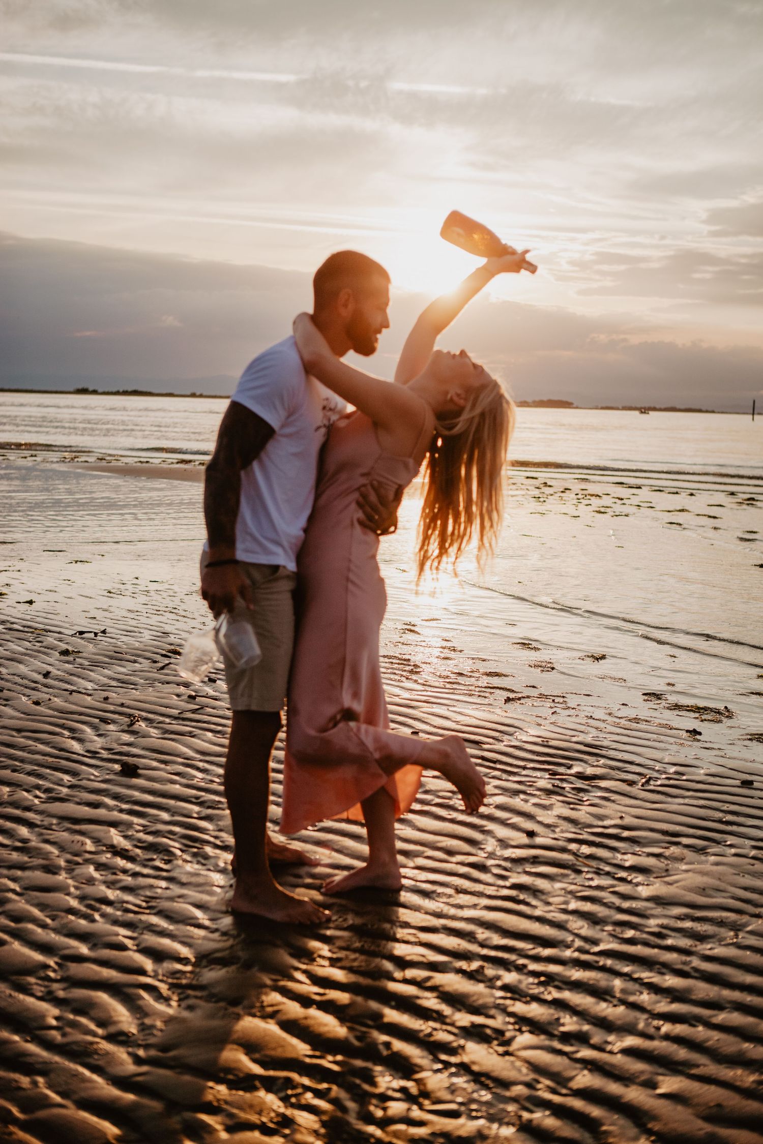 Couple embracing on beach at sunset with dramatic sky.