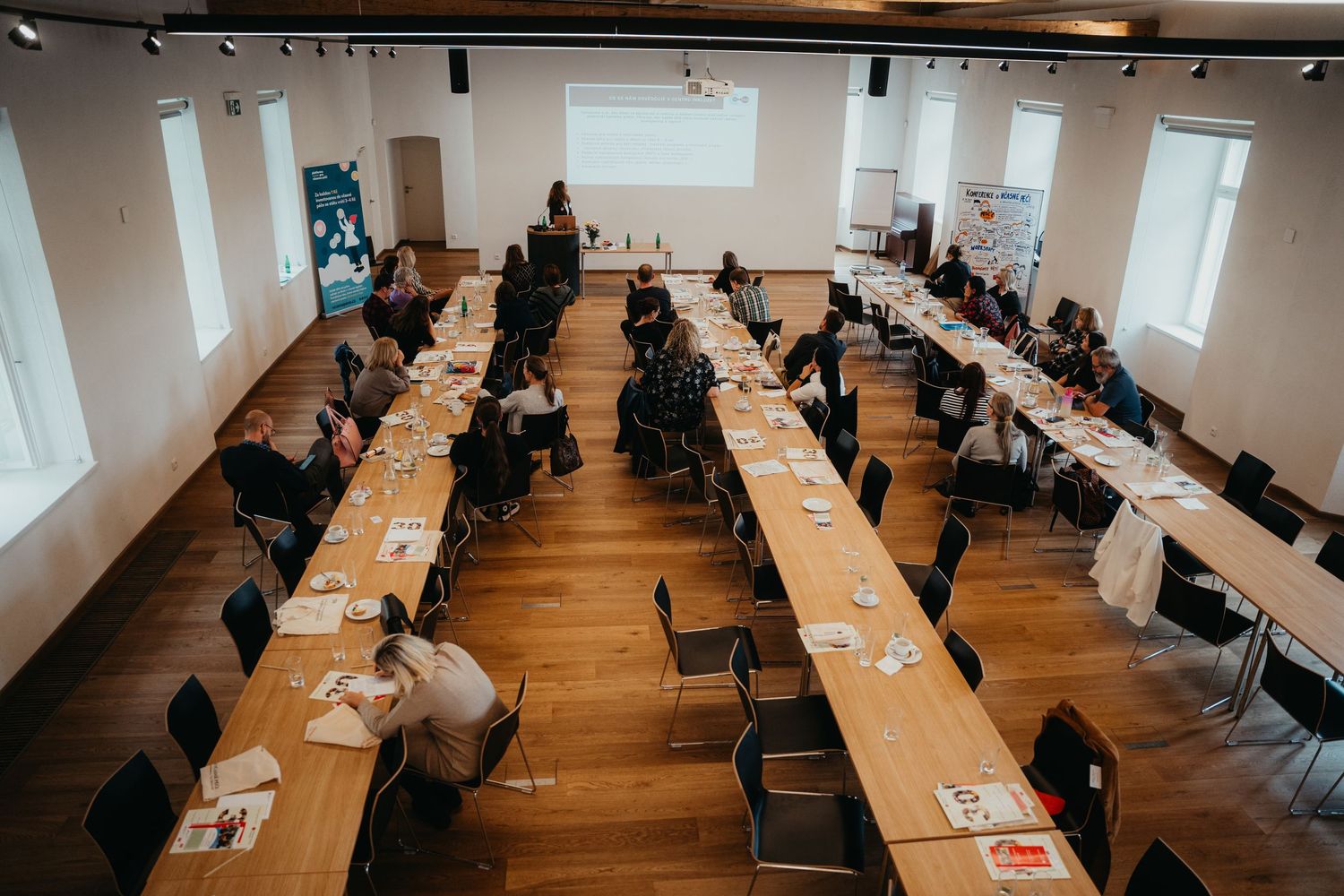 Students working at long tables in a modern classroom with wooden floors and white walls during an examination period.